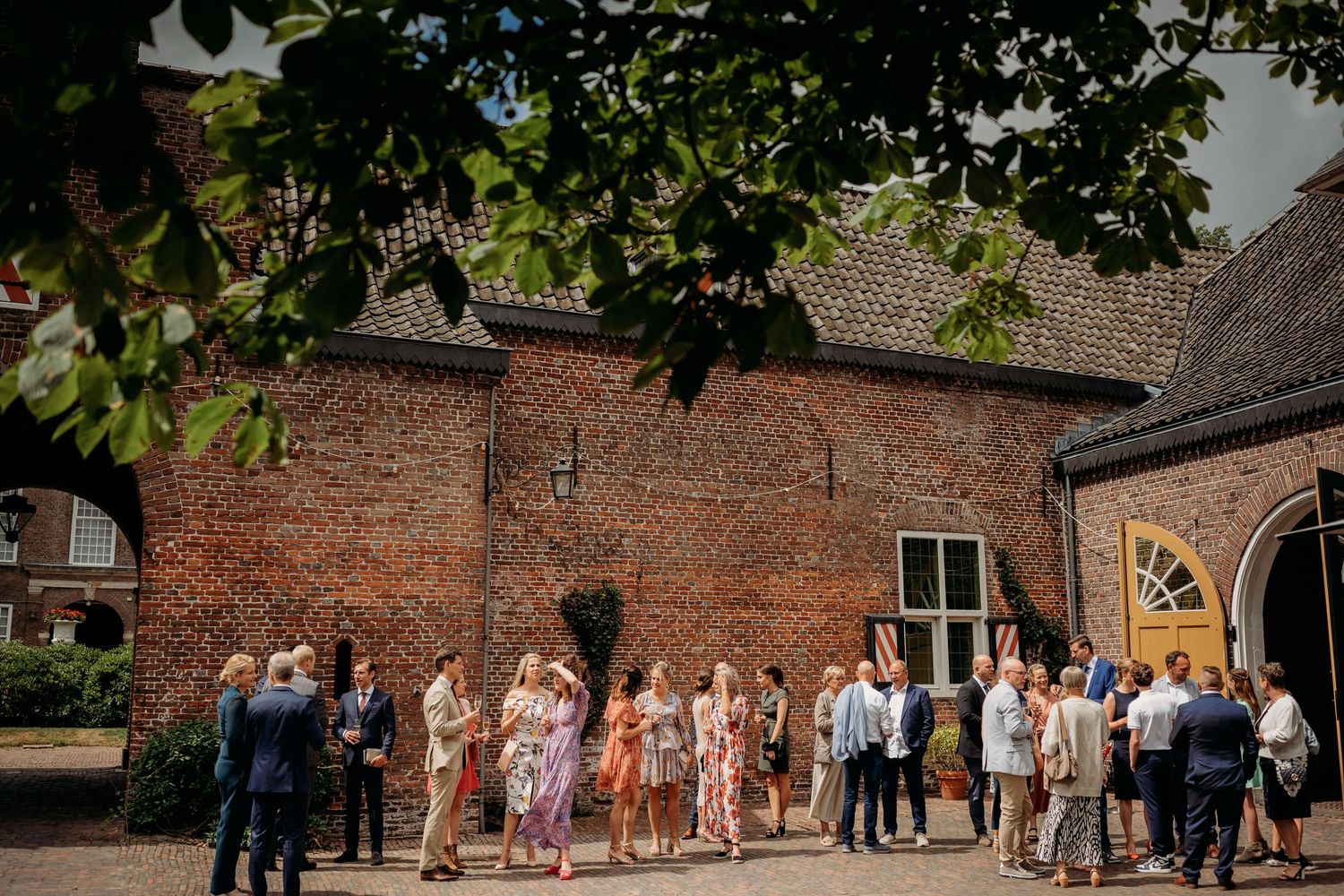Wedding guests mingling outside a rustic brick venue on a sunny day.