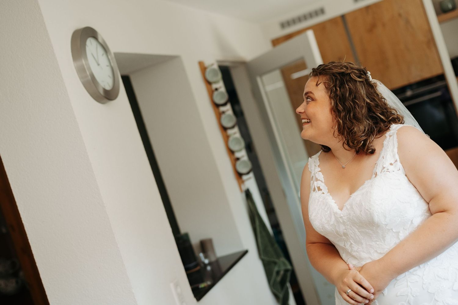 Bride in white lace wedding dress smiling in a bright room on her wedding day.
