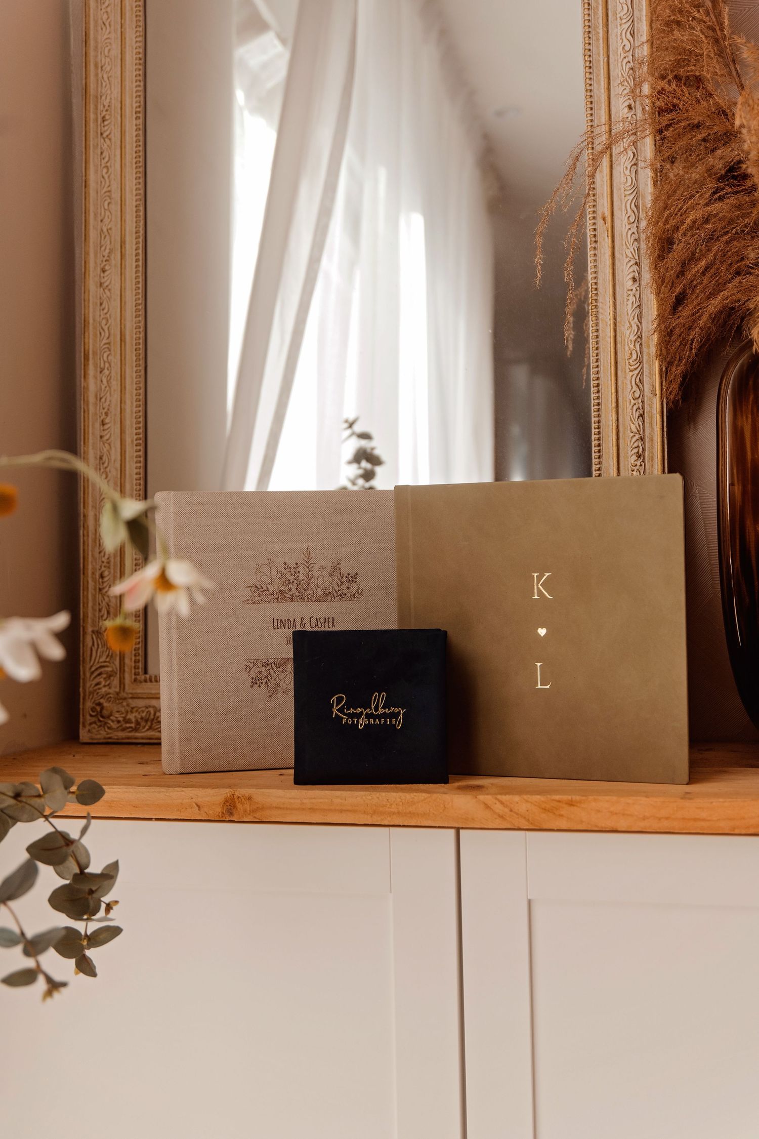 Trouwfotoalbums en enveloppen artistiek gerangschikt op witte plank met gouden spiegel, branding fotografie Brabant