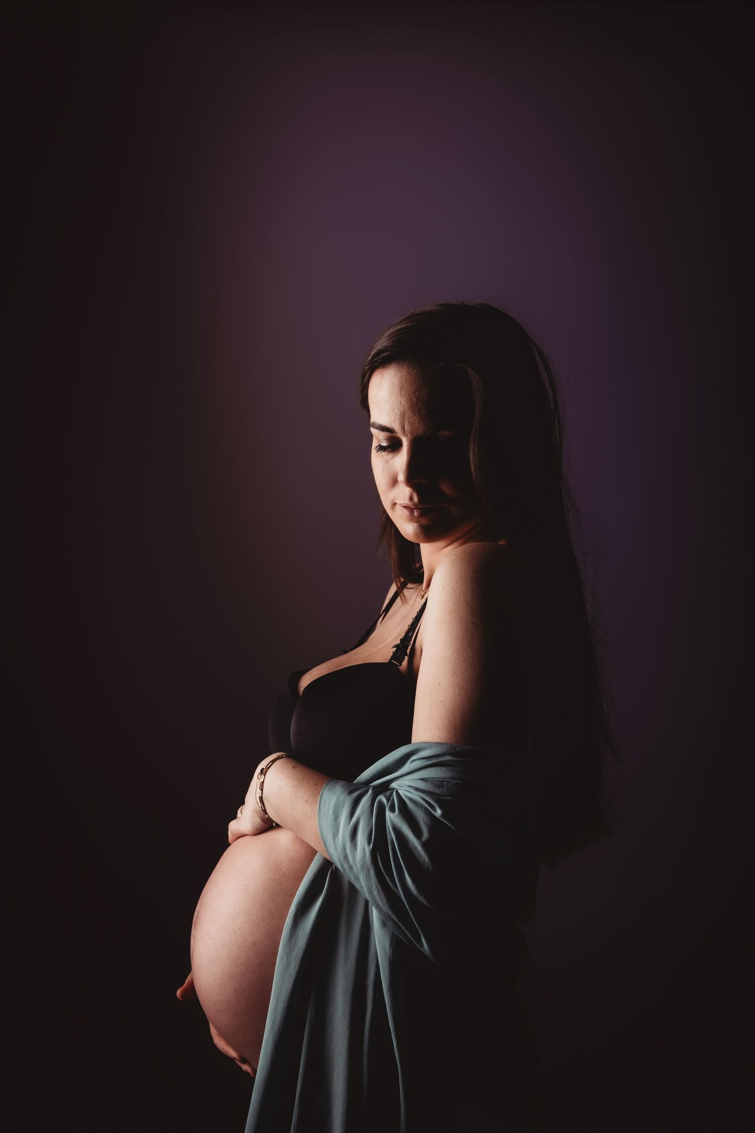 Artistieke zwangerschapsfoto silhouet van zwangere vrouw in blauwe jurk tegen donkere achtergrond, zwangerschapsfotografie Brabant
