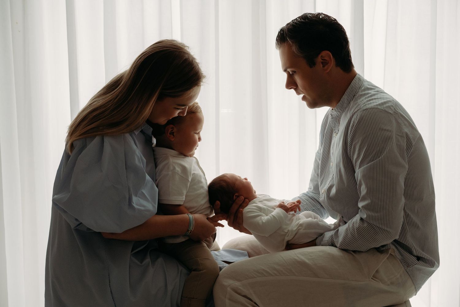 Familie verzameld rond pasgeboren baby bij raam, newbornfotografie Brabant