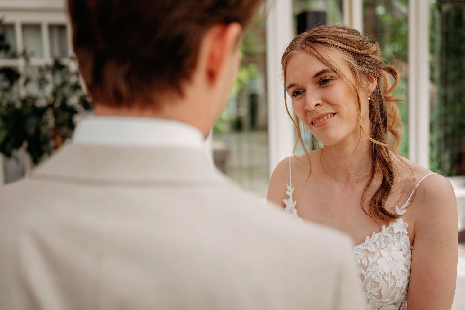Bride smiling warmly at groom during wedding ceremony, wearing lace dress with elegant updo hairstyle.
