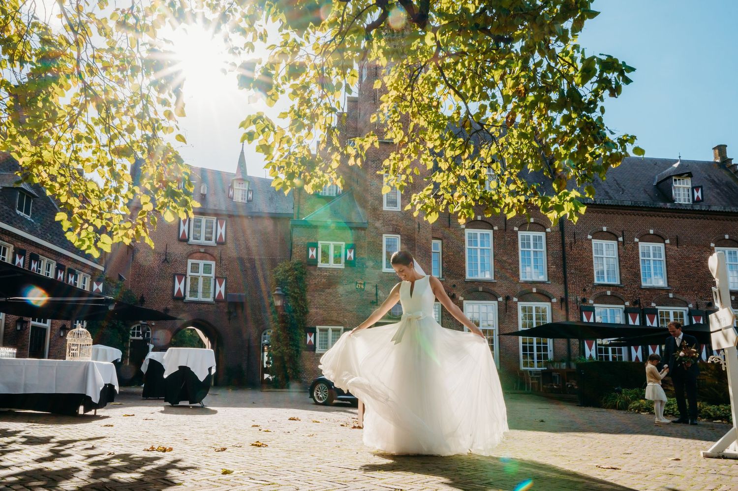 Buitenceremonie bij zonovergoten locatie met bomen en gebouwen, bruidsfotografie Kasteel Maurick Vught, Brabant.