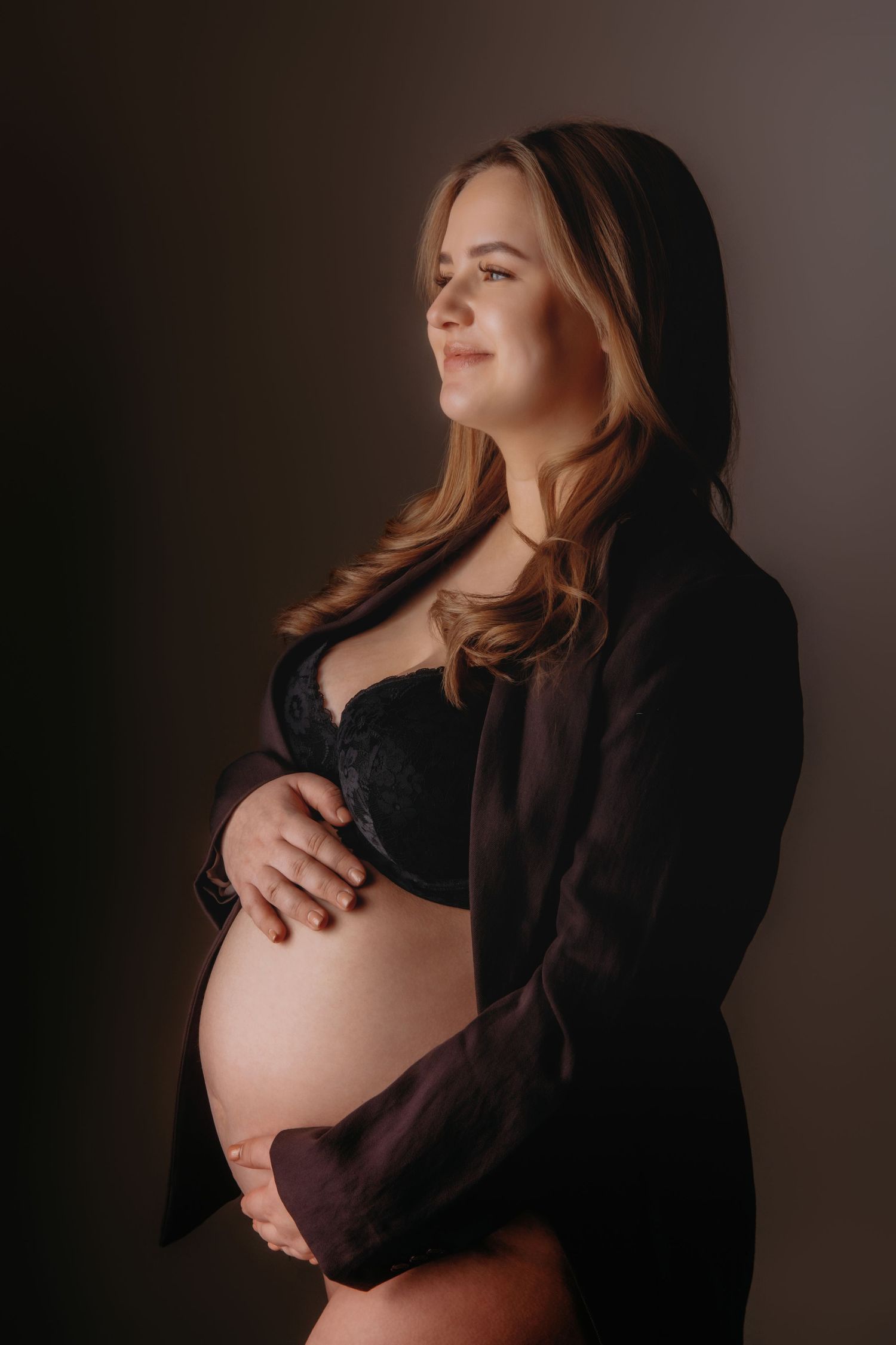 Zwangerschapsfotoshoot van vrouw in donkere trui in sfeervolle belichting, zwangerschapsfotografie Brabant