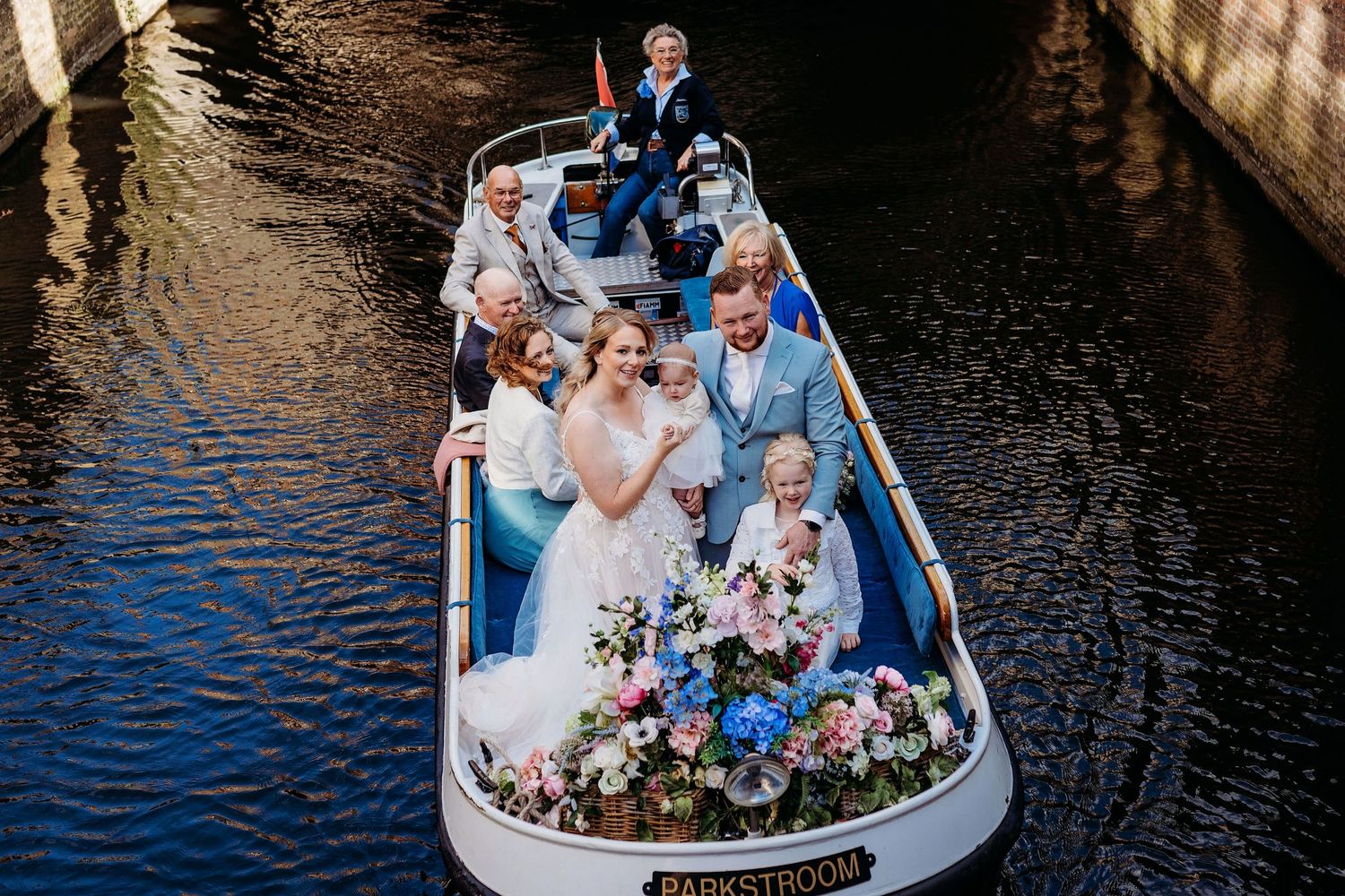 Romantische boottocht met bruidspaar en gasten op rustig water, spontane bruidsfotografie in Den Bosch en omgeving Brabant.