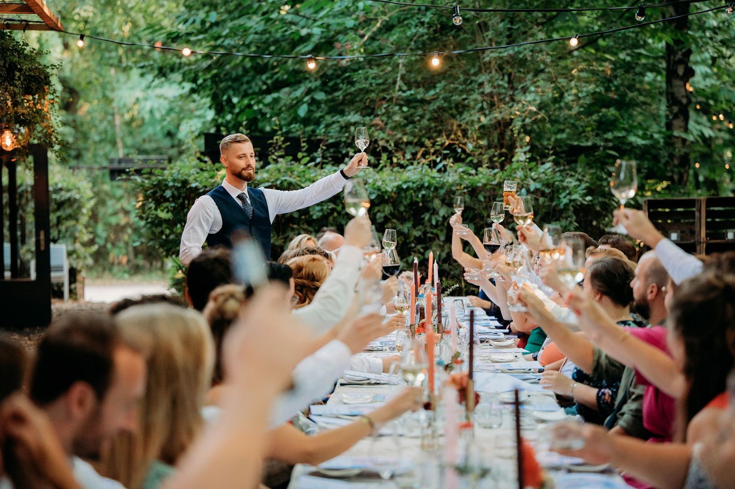 Gasten proosten samen tijdens diner in de buitenlucht bij bruiloft in Brabant, warme en spontane fotografie
