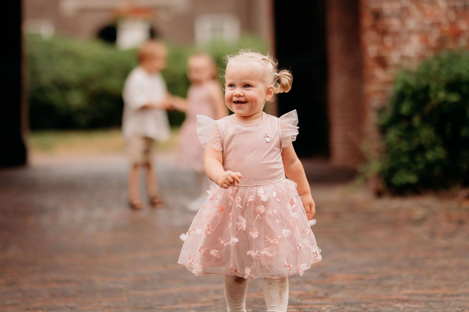 Happy toddler girl in pink tutu dress smiling outdoors at a wedding celebration.