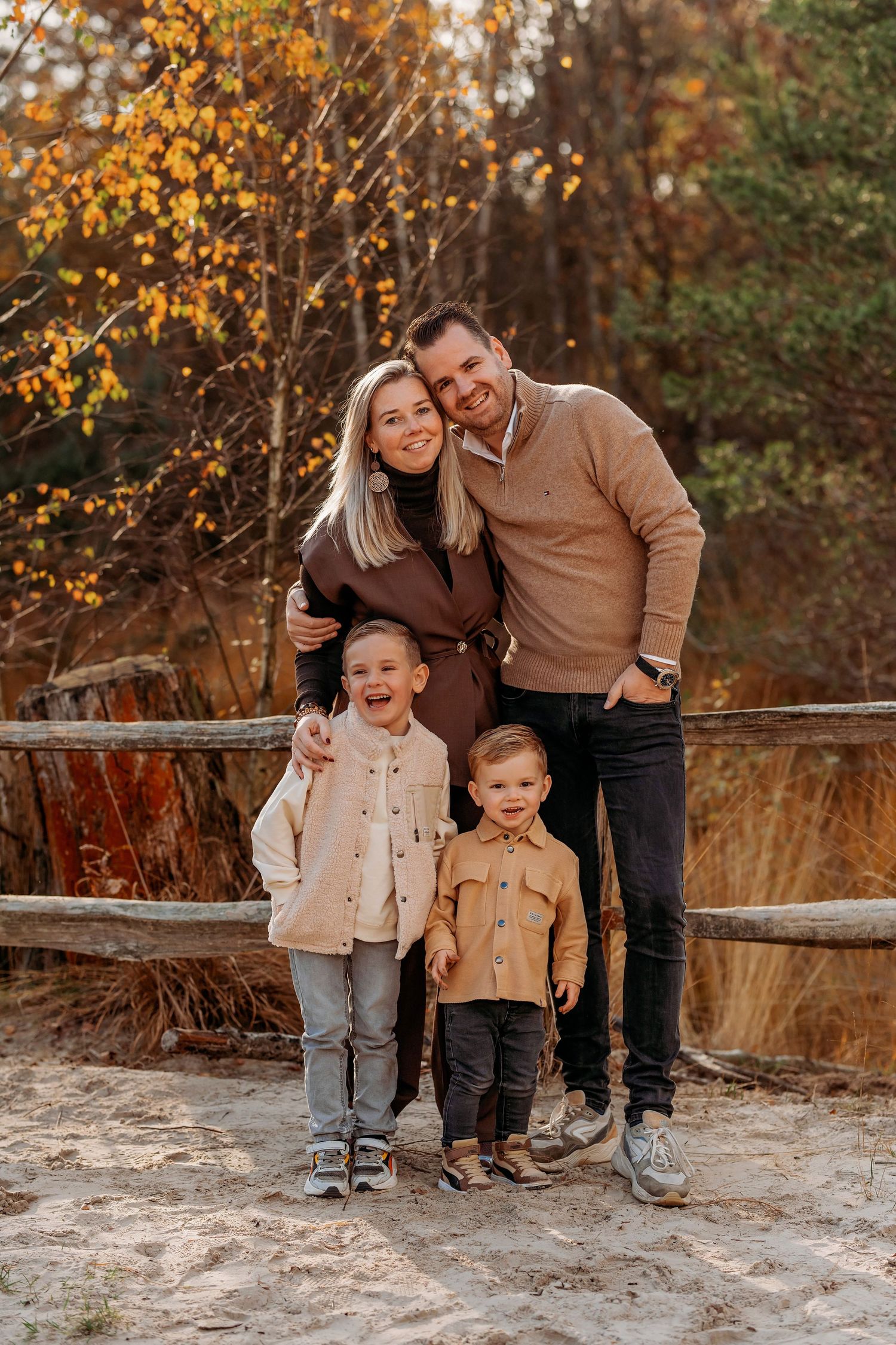 Candid familiefoto met speelse interacties bij herfstscenery en houten hek, familieshoot Brabant