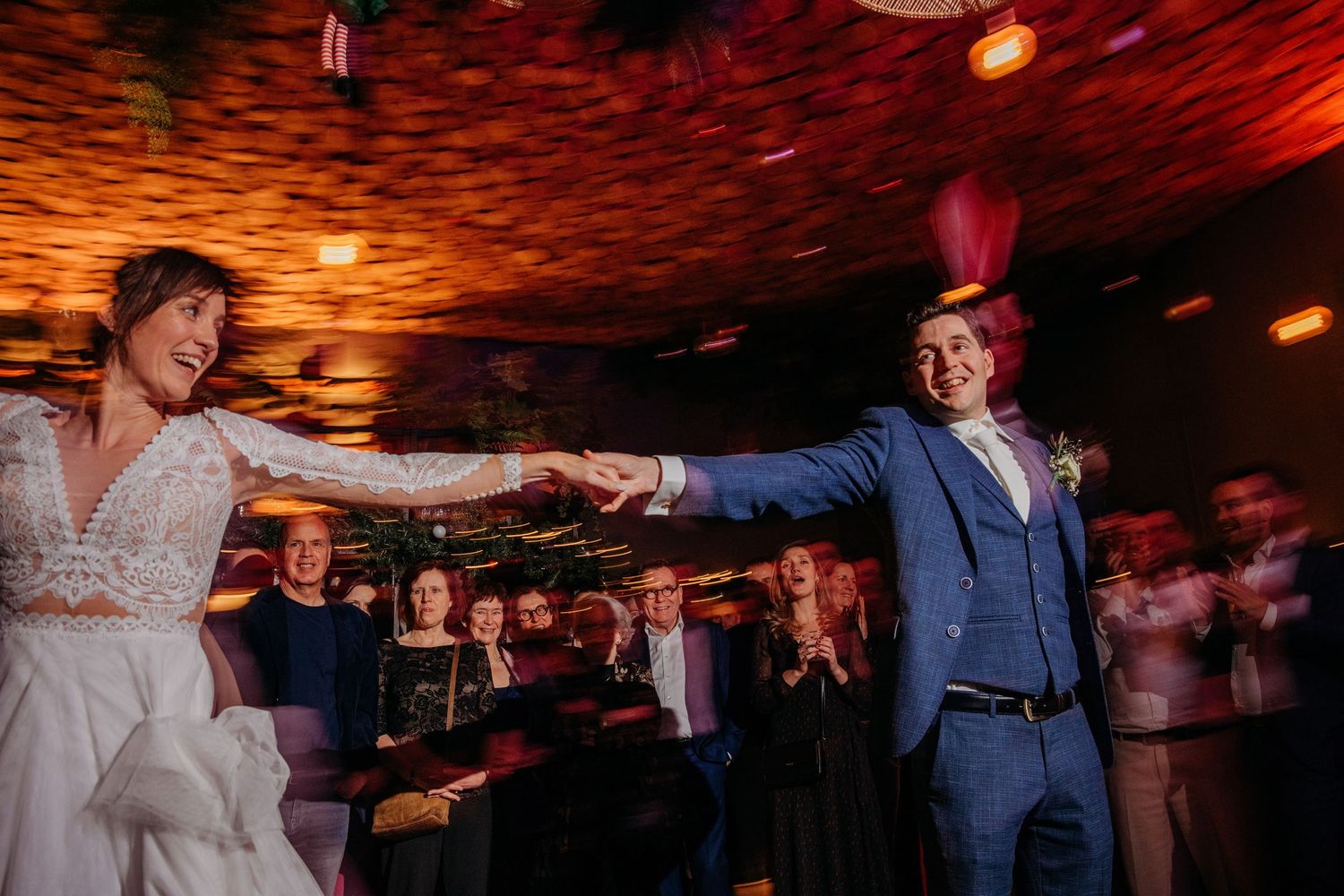 Bruiloftsgasten dansen op feestvloer met rood sfeerlicht, spontane bruidsfotografie bij Boscafé Oisterwijk, regio Brabant.