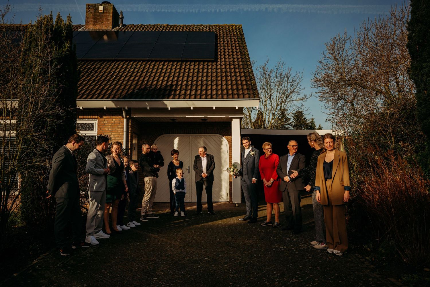Gasten verzamelen buiten bij bakstenen pand met zonnepanelen op zonnige winterdag, bruidsfotografie bij Boscafé Oisterwijk, Brabant.