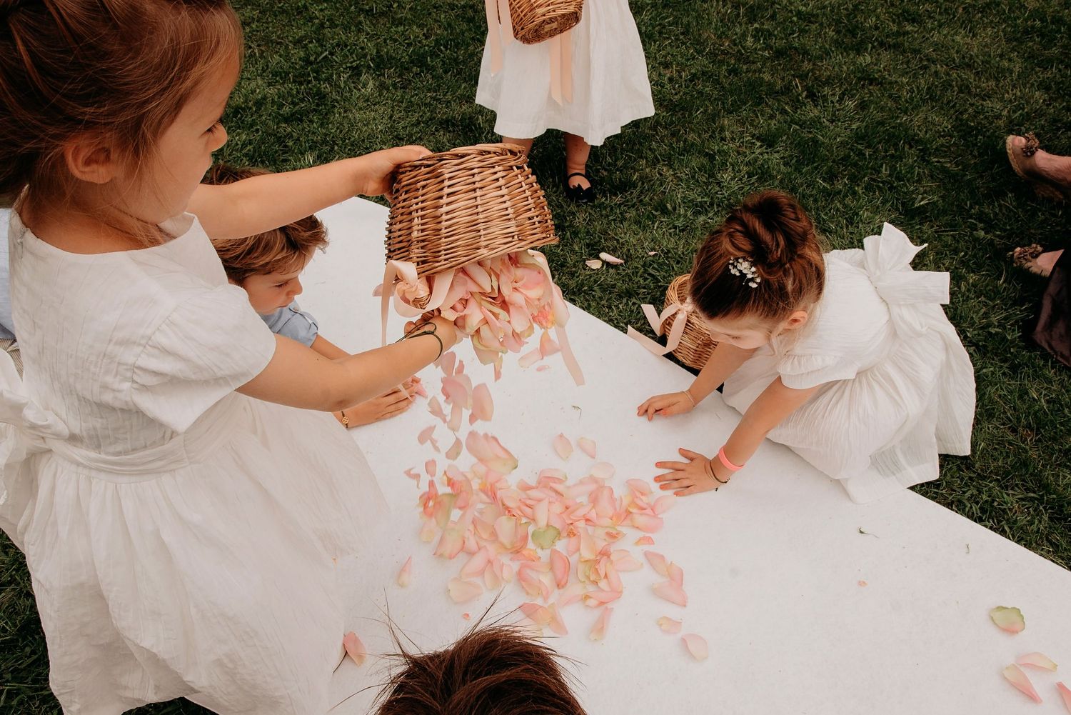 Kinderen zittend rond wit tafelkleed met roze bloemblaadjes, trouwfotografie Brabant.