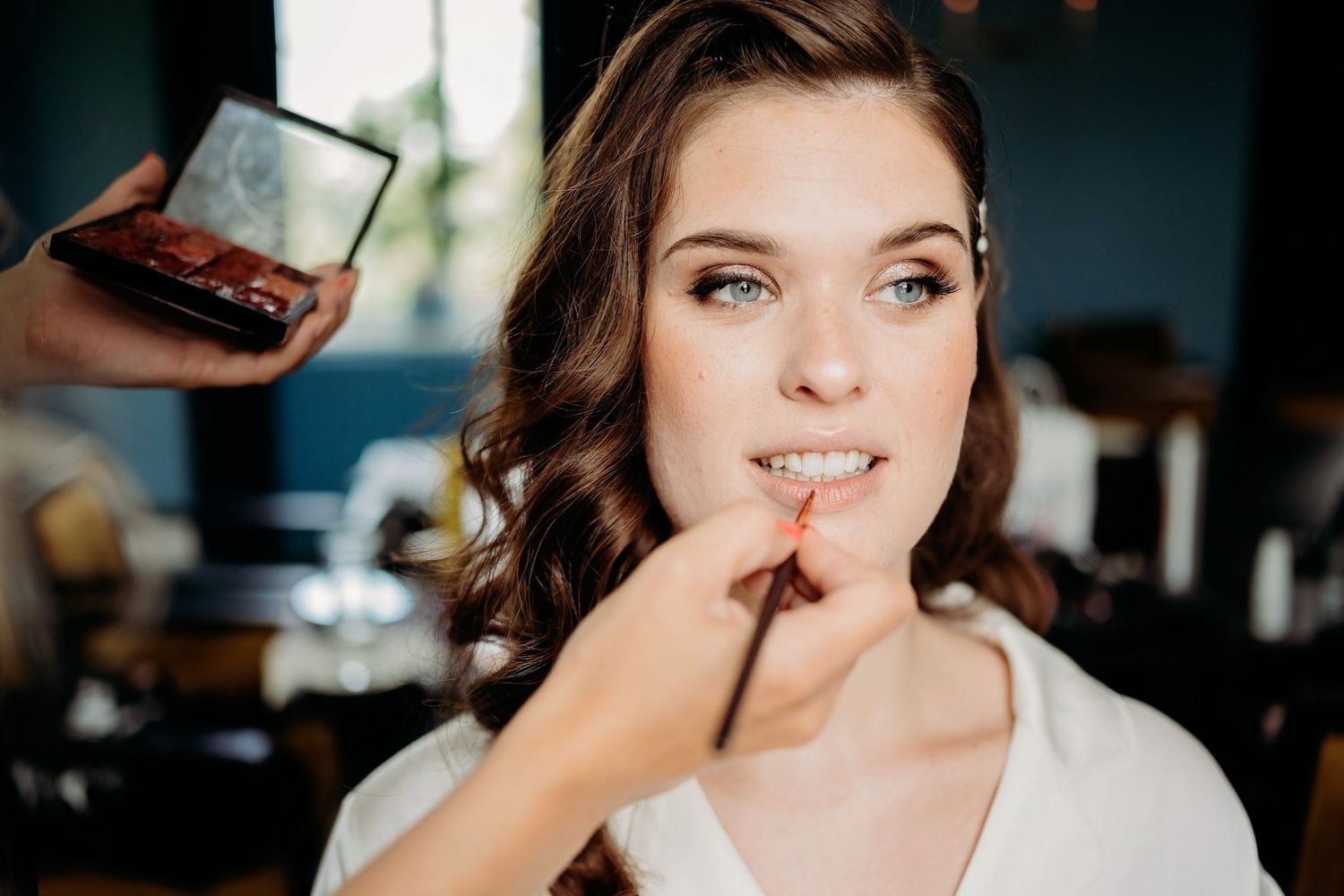 Make-up artiest brengt lipstick aan bij de bruid, natuurlijk licht en intiem moment, Den Bosch.