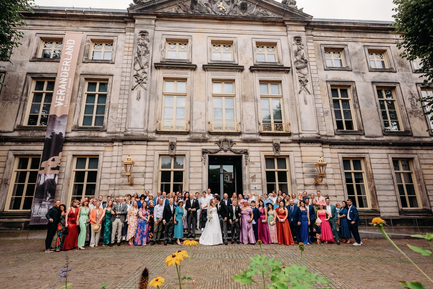 Grote groep in formele kleding poseert buiten historische gevel, bruidsfotografie Noordbrabants Museum Den Bosch, Brabant.