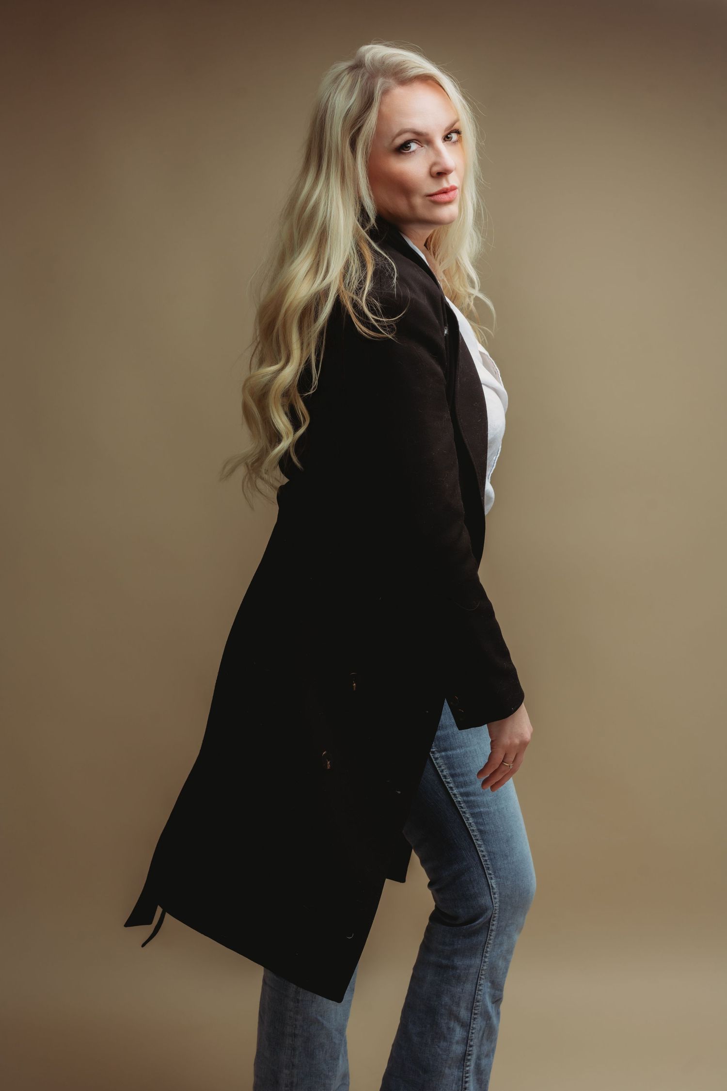 Stijlvol zwart blazer en jeans outfit gefotografeerd tegen beige studioachtergrond, portretfotografie Brabant