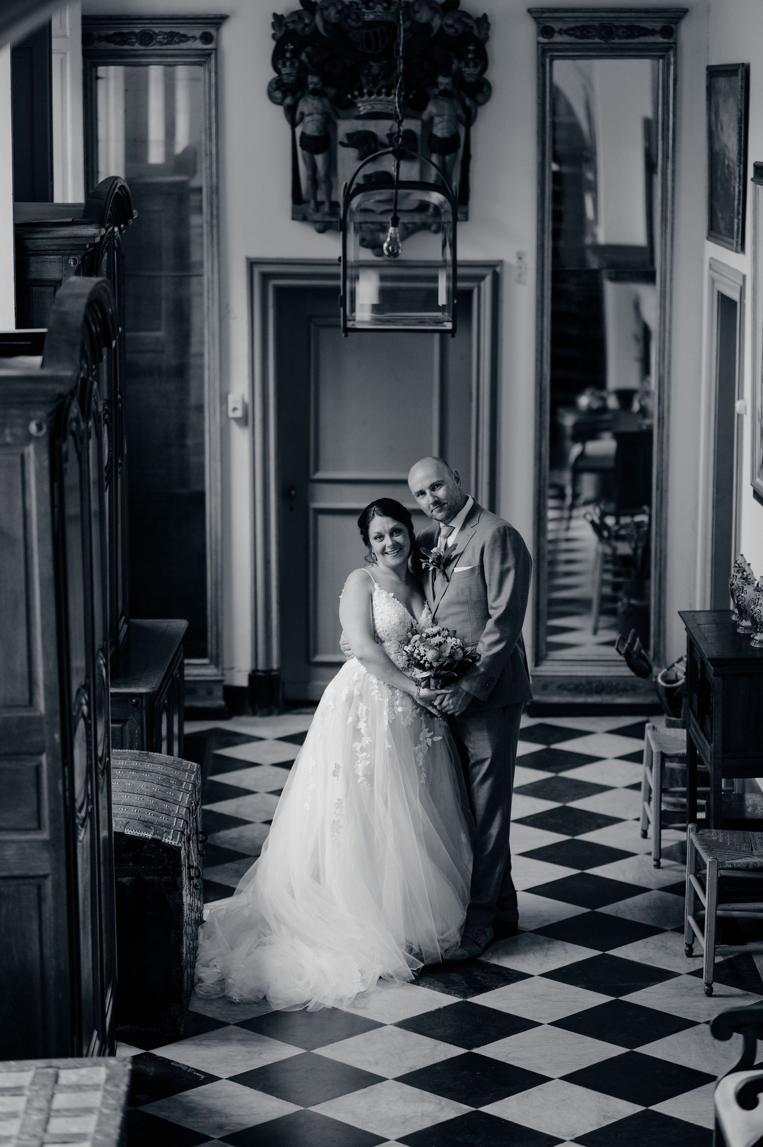 Black and white wedding portrait of bride and groom embracing in elegant hall with checkered floor.