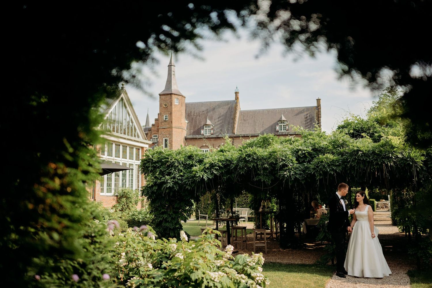 Bruidspaar staat in weelderige tuin met historische architectuur en omlijst groen, bruidsfotografie Brabant