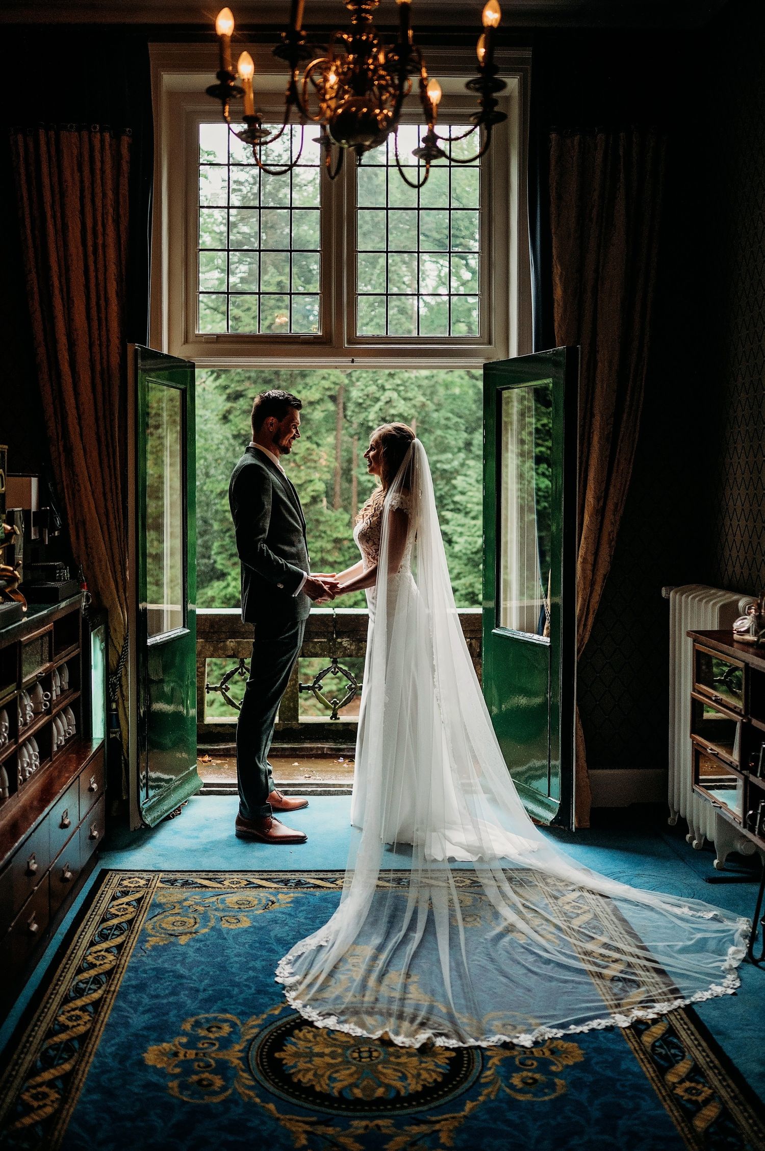 Bruidspaar silhouet bij grote ramen in elegante zaal met blauw tapijt, bruidsfotografie Huize Bergen Vught, Brabant.
