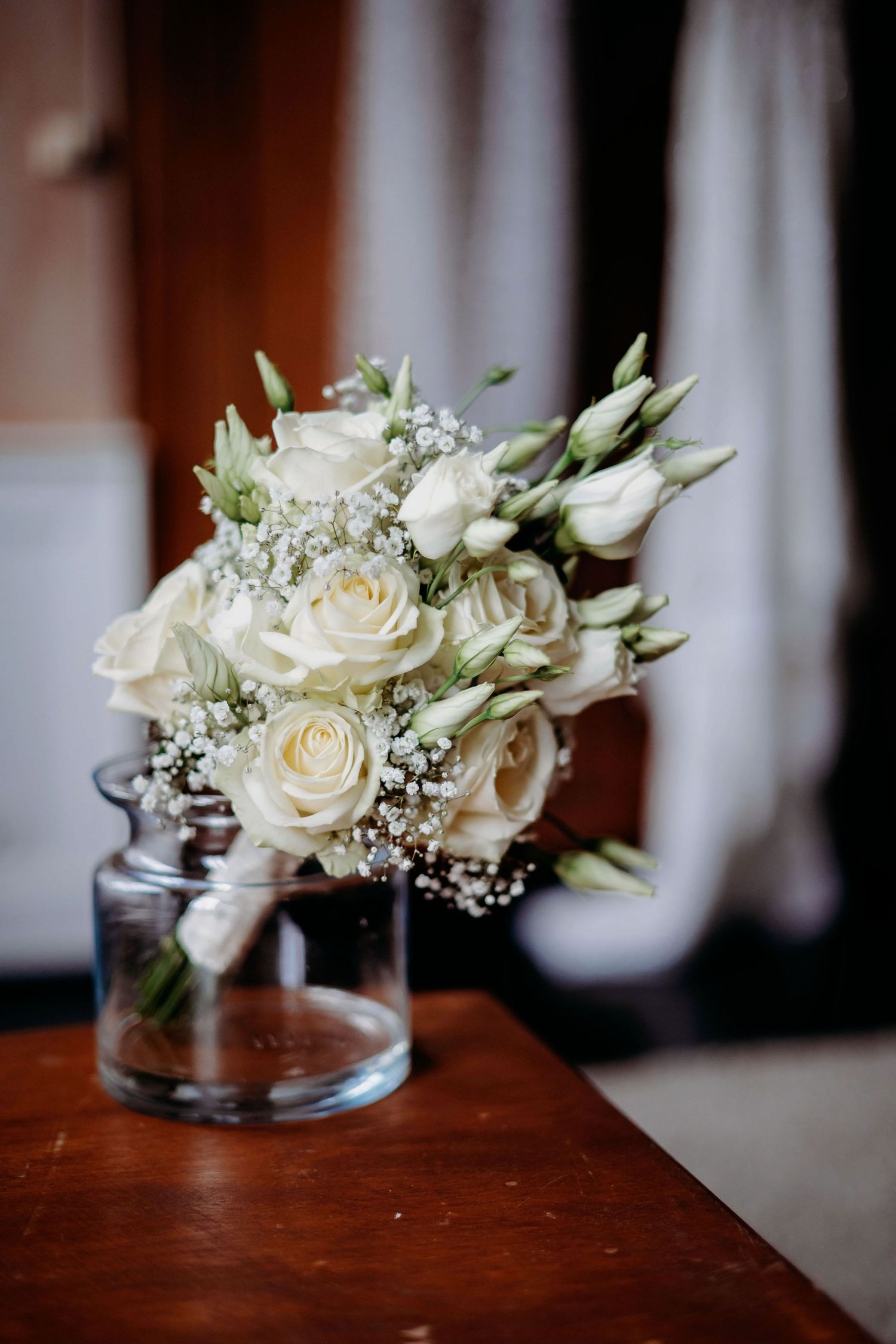 Witte rozen en baby's breath bloemstuk in glazen vaas op houten oppervlak, bruidsfotografie Brabant
