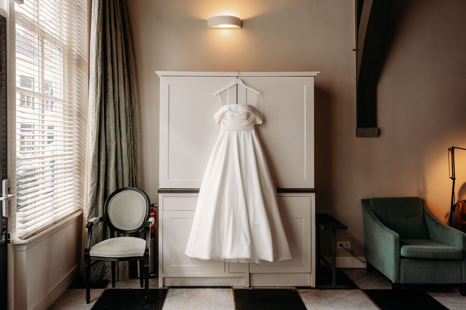 Witte trouwjurk elegant opgehangen bij raam in hotelkamer, bruidsfotografie Noordbrabants Museum Den Bosch, Brabant.