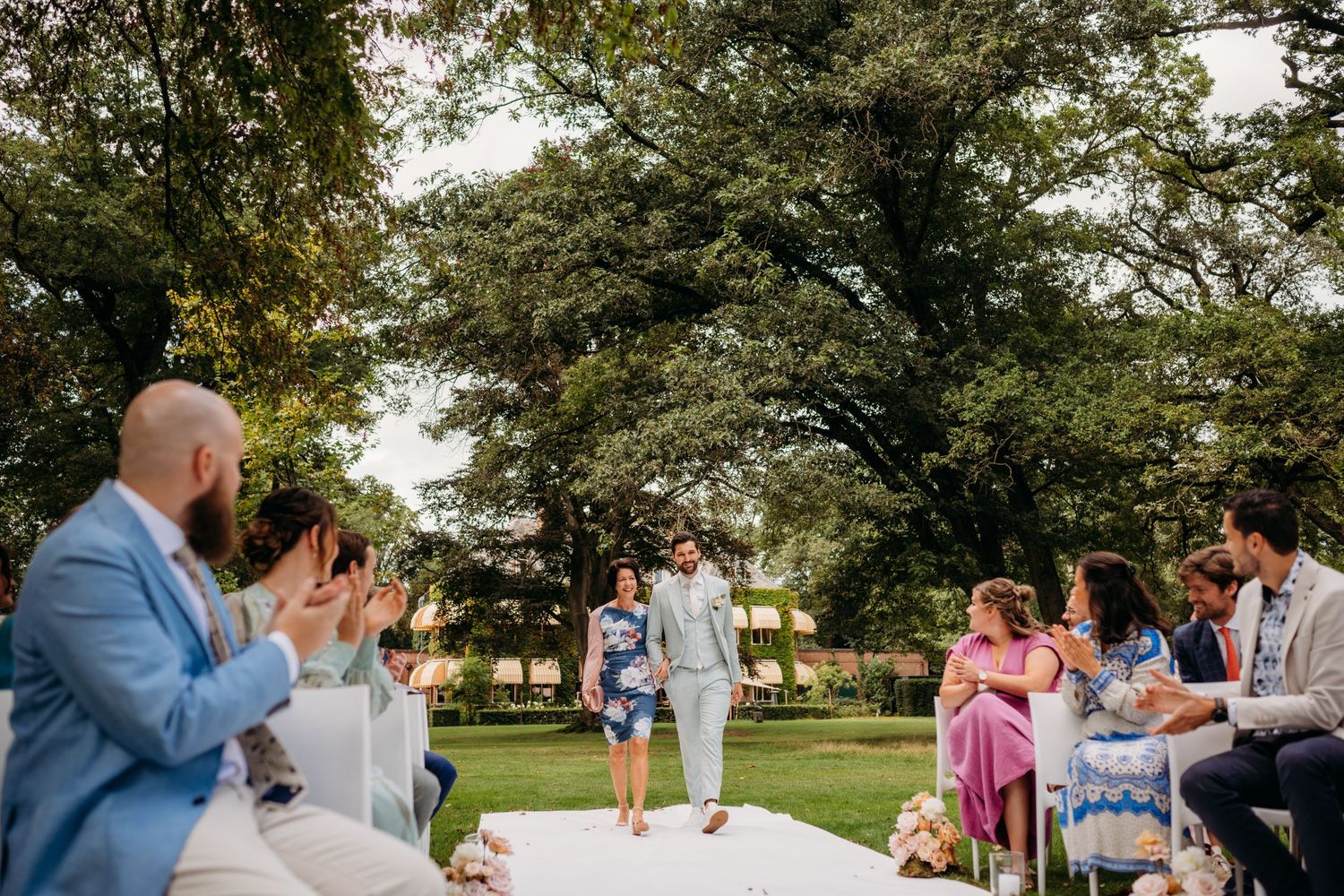 Bruiloftsgasten applaudisseren tijdens een buitenceremonie in de tuin, authentiek moment Den Bosch.