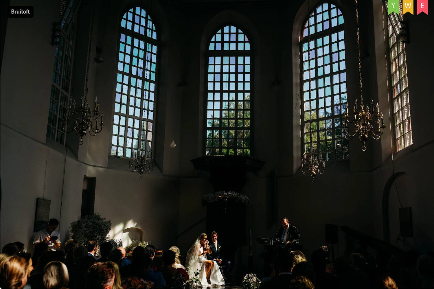 Kerkinterieur met bogen die natuurlijk licht werpen over verzamelde gasten, bruidsfotografie Brabant