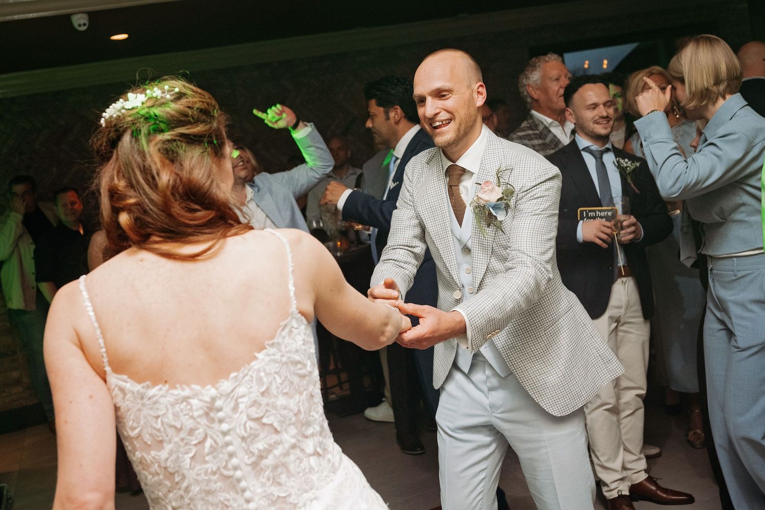 Bride and groom dance joyfully together at their wedding reception surrounded by guests.