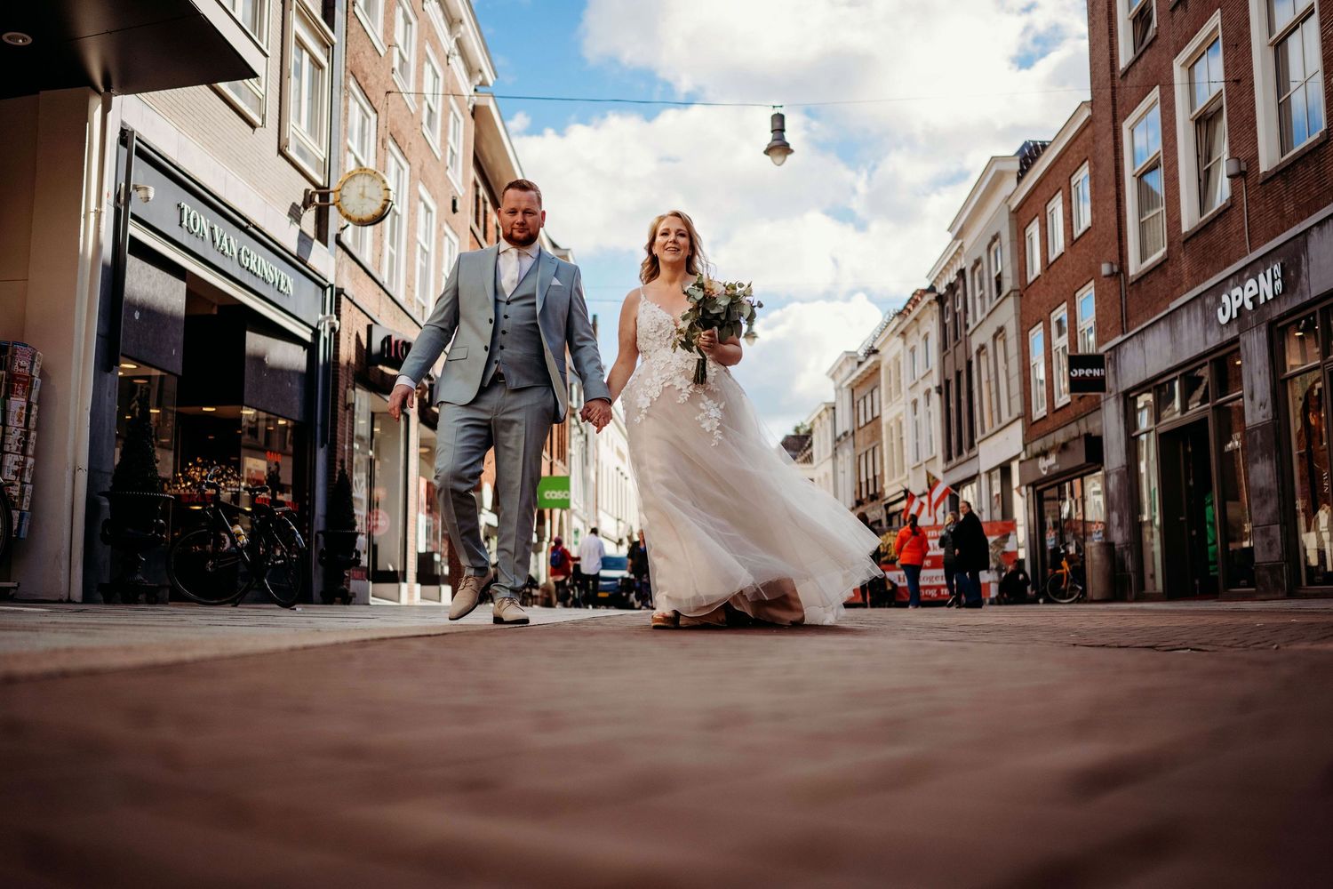 Bruiloftsfeest gefotografeerd vanuit laag standpunt in sfeervolle straat, spontane bruidsfotografie in Den Bosch en Brabant.