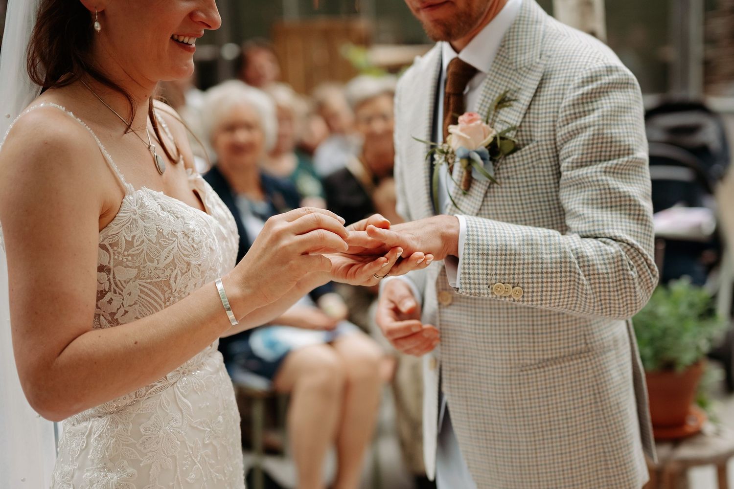 Bride and groom exchanging rings during wedding ceremony, with guests seated in the background.
