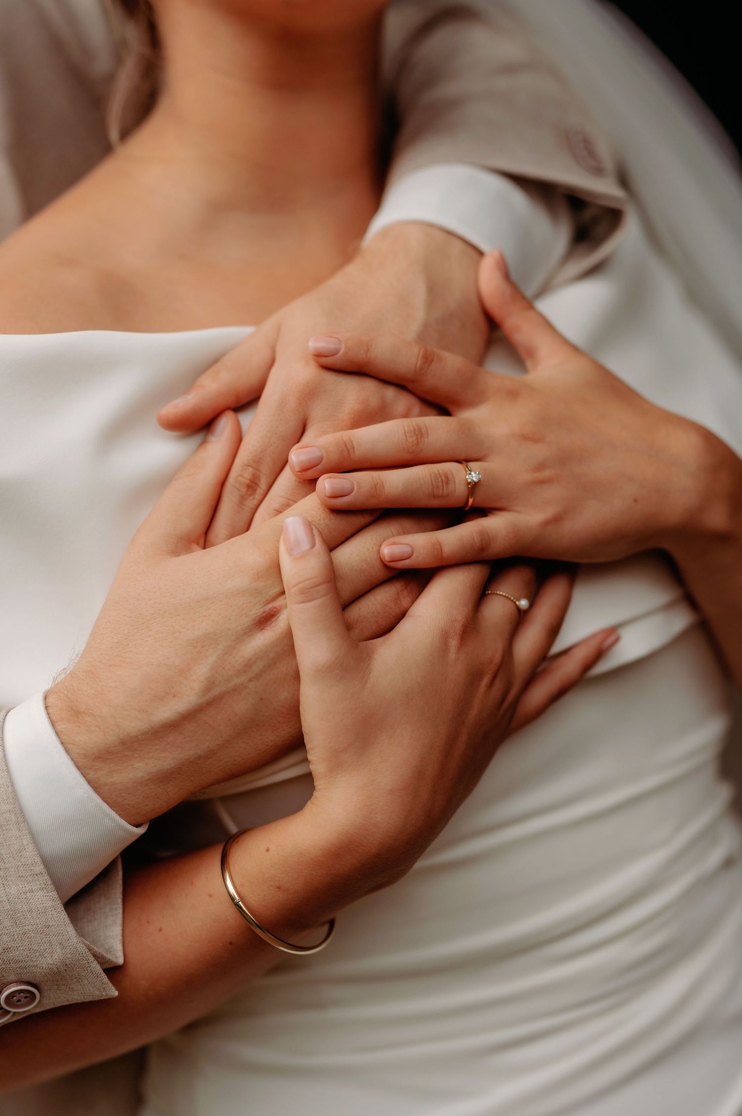 Bride and groom holding hands together showing wedding rings and gold bracelet in an intimate close-up photo.
