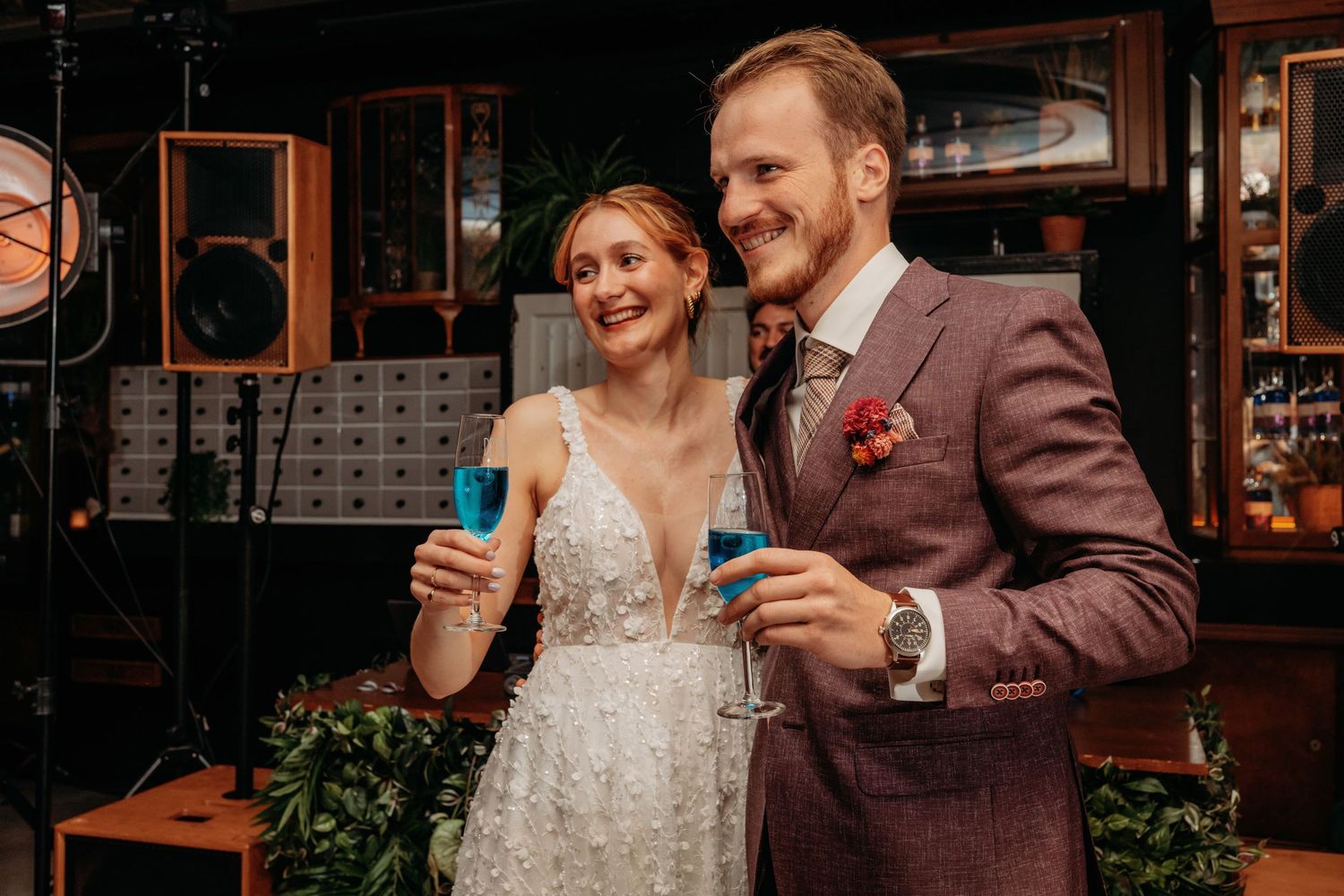 Bruidspaar proost samen in een sfeervolle bar tijdens hun trouwdag, warme en spontane trouwfotografie