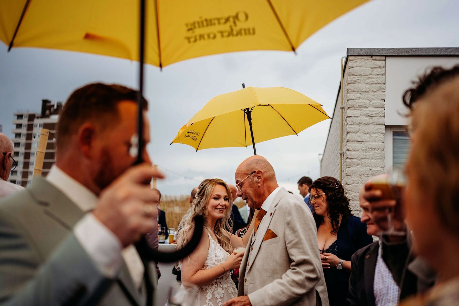 Bruiloftsgasten met gele paraplu’s in de regen, spontane bruidsfotografie tijdens buitenbruiloft in Den Bosch en Brabant.