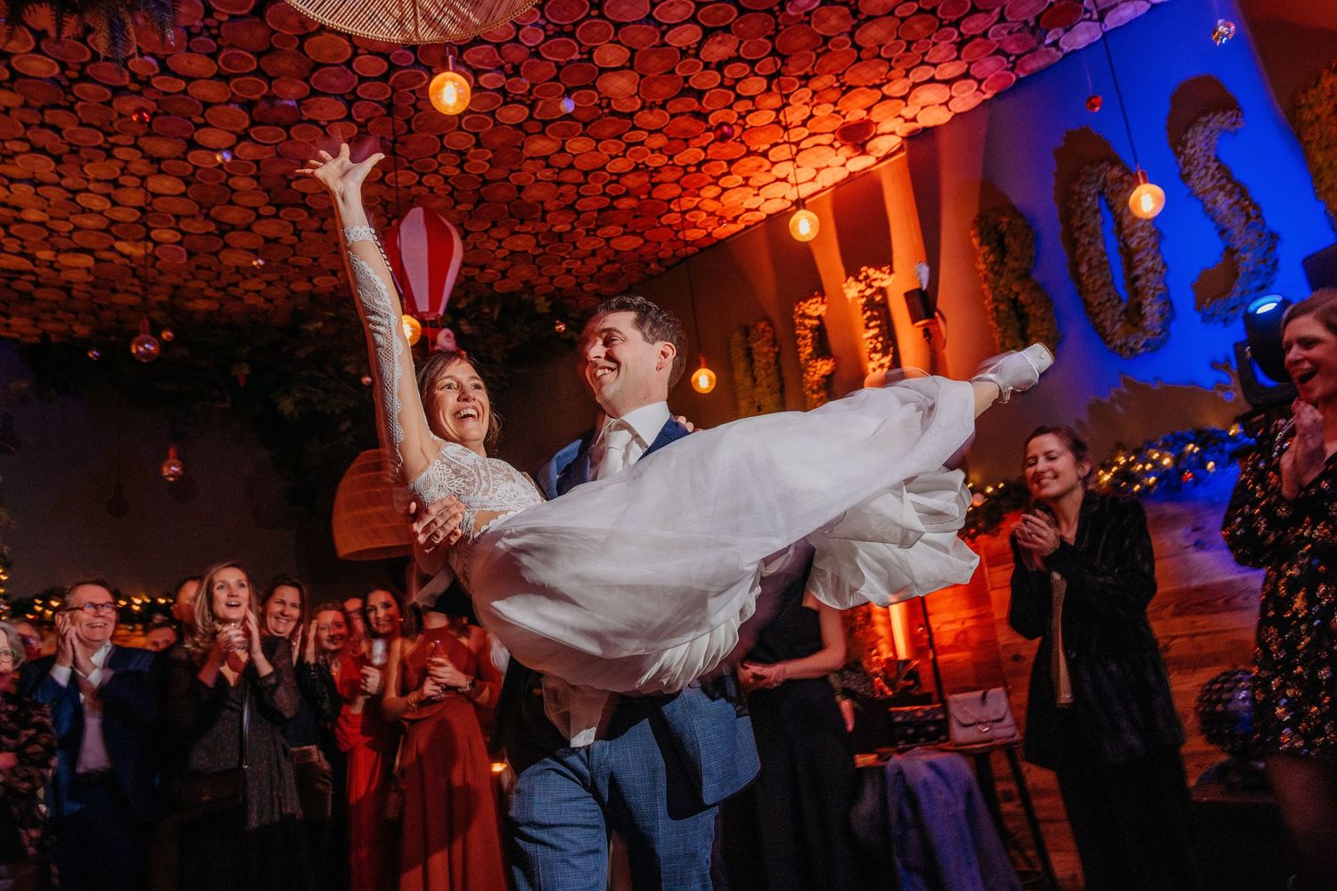 Speelse danslift tijdens trouwfeest met rood licht, spontane bruidsfotografie bij Boscafé Oisterwijk, regio Brabant.