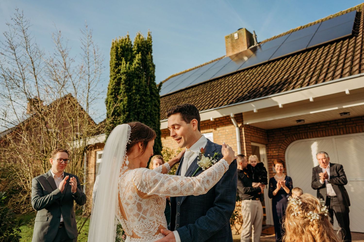 Bruidspaar deelt eerste dans buiten met gasten bij huis met zonnepanelen, romantische bruidsfotografie bij Boscafé Oisterwijk, Brabant.