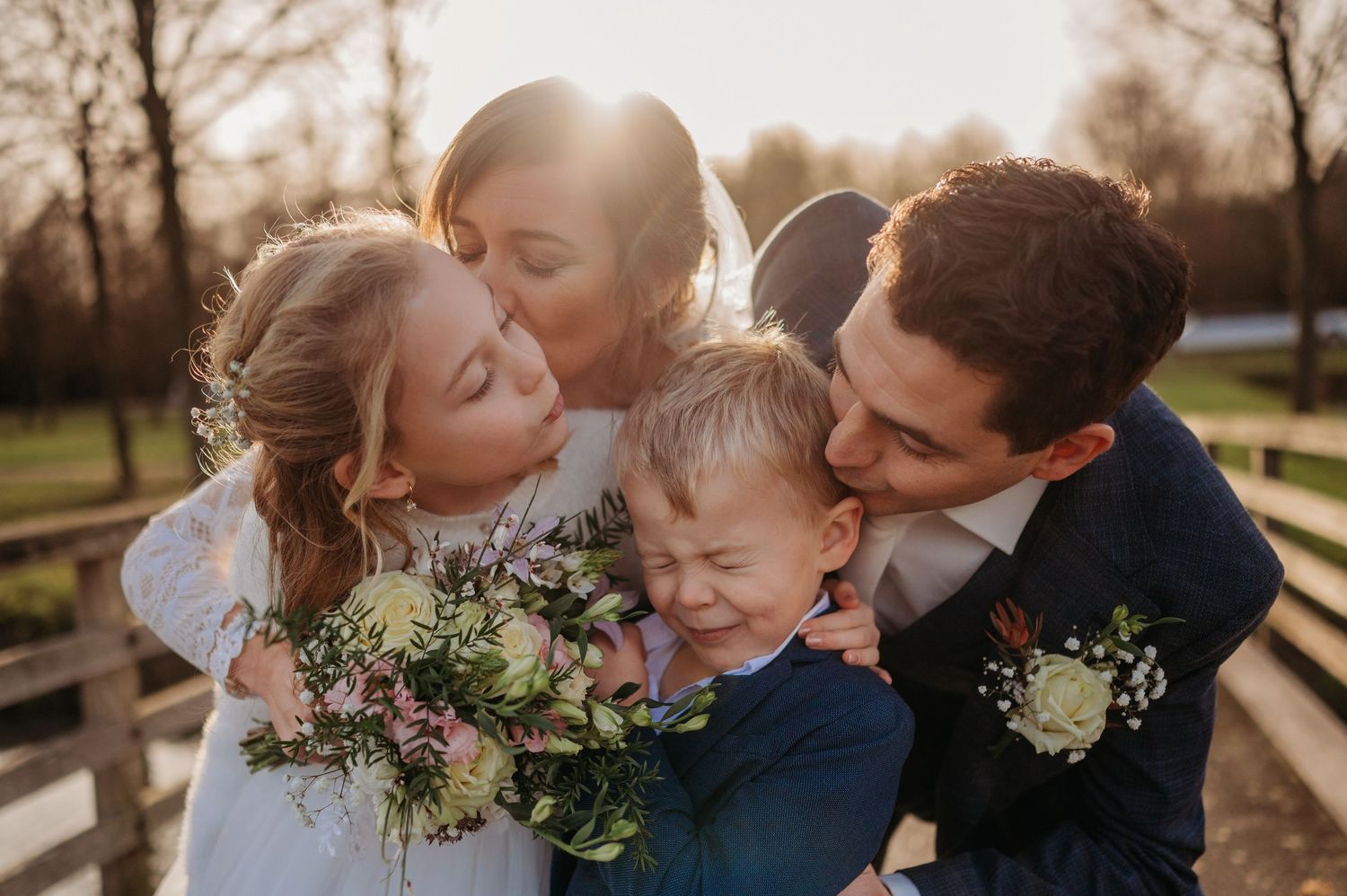 Familie deelt intieme omhelzing bij zonsondergang met bloemen, spontane bruidsfotografie bij Boscafé Oisterwijk, Brabant.