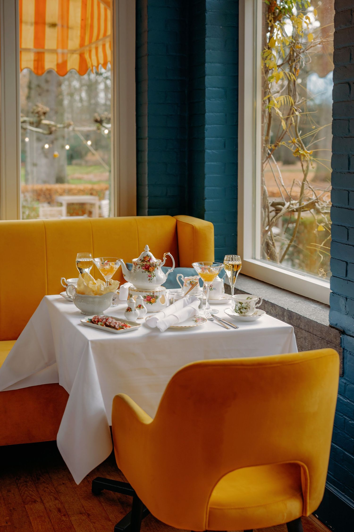 Elegante eetkamer met gele fluwelen banken en witte tafelkleden bij zonovergoten ramen, interieurfotografie Brabant