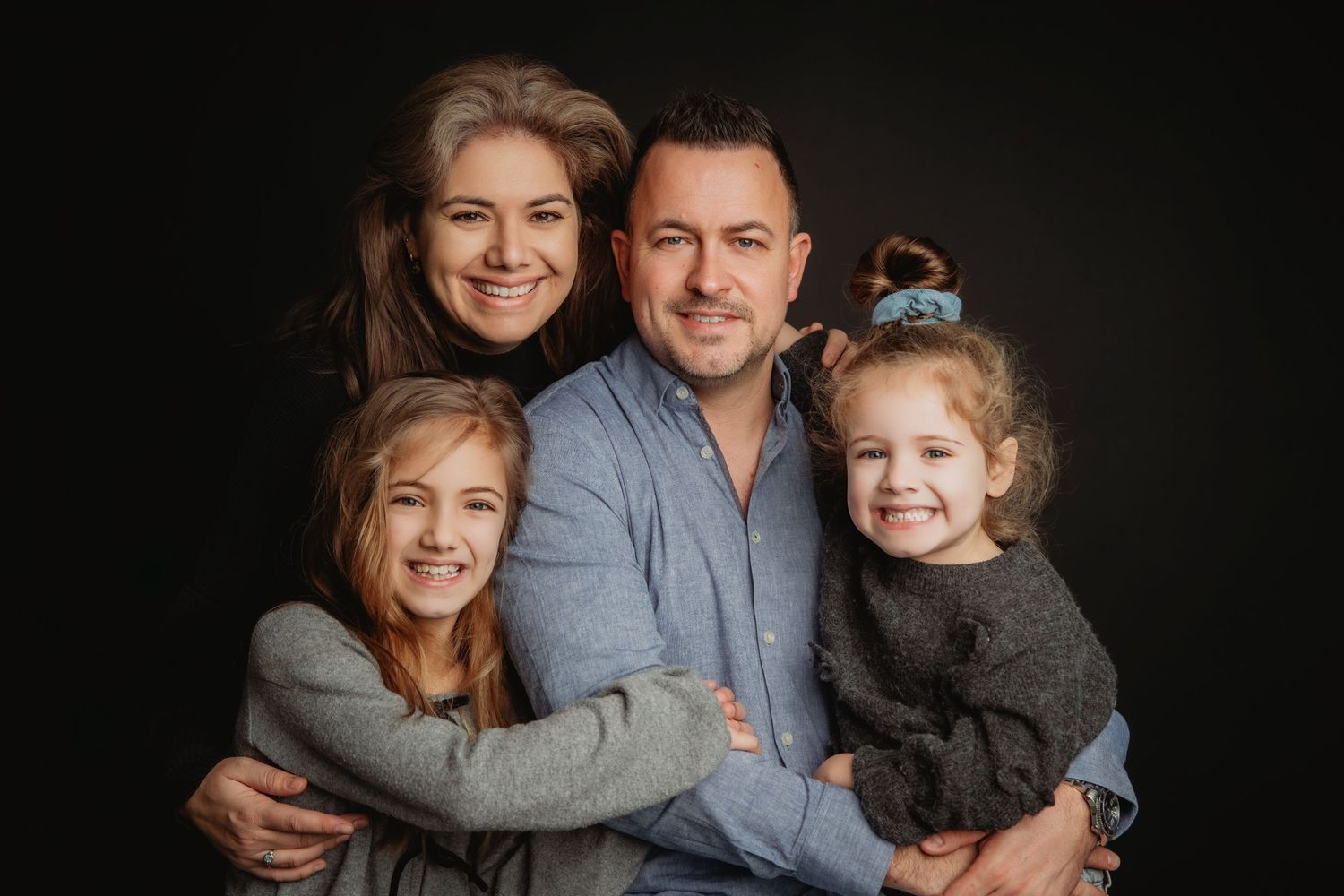 Warme familiefoto tegen donkere achtergrond met liefdevolle omhelzingen en glimlachen, familieshoot Brabant