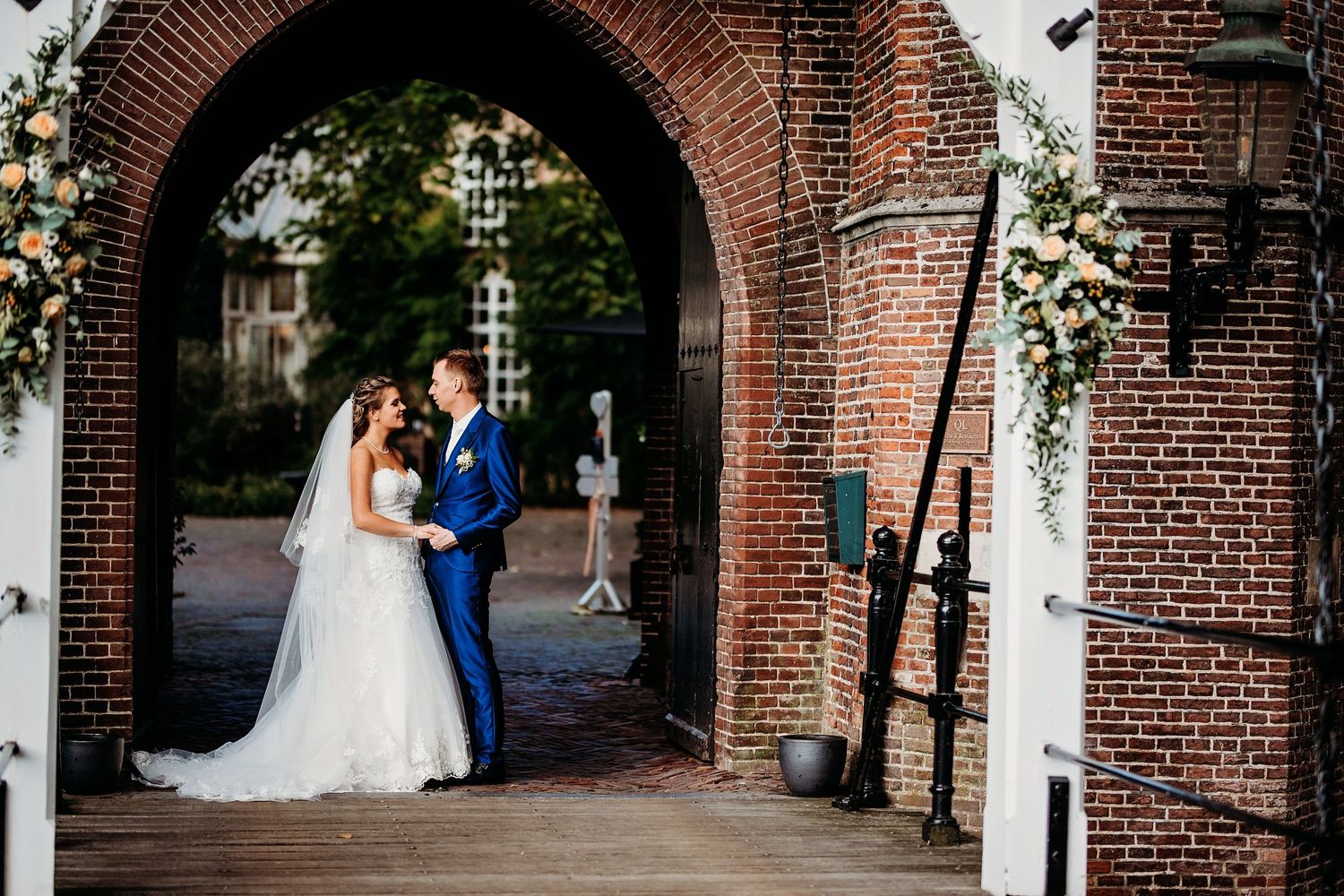 Bruidspaar in elegante bakstenen boog in tuin, bruidsfotografie Kasteel Maurick Vught, Brabant.