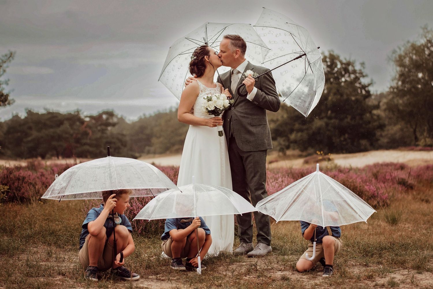 Trouwkoppel poseert met witte parasols in romantische buitensetting, bruidsfotografie Brabant.
