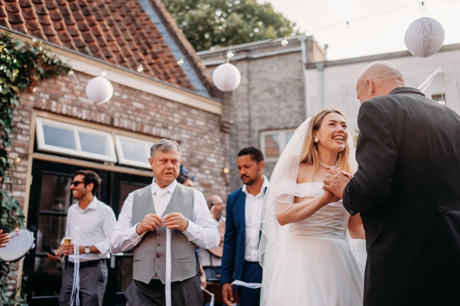 Candid moment van receptie met gasten die vieren voor bakstenen gebouw, bruidsfotografie Noordbrabants Museum Den Bosch, Brabant.