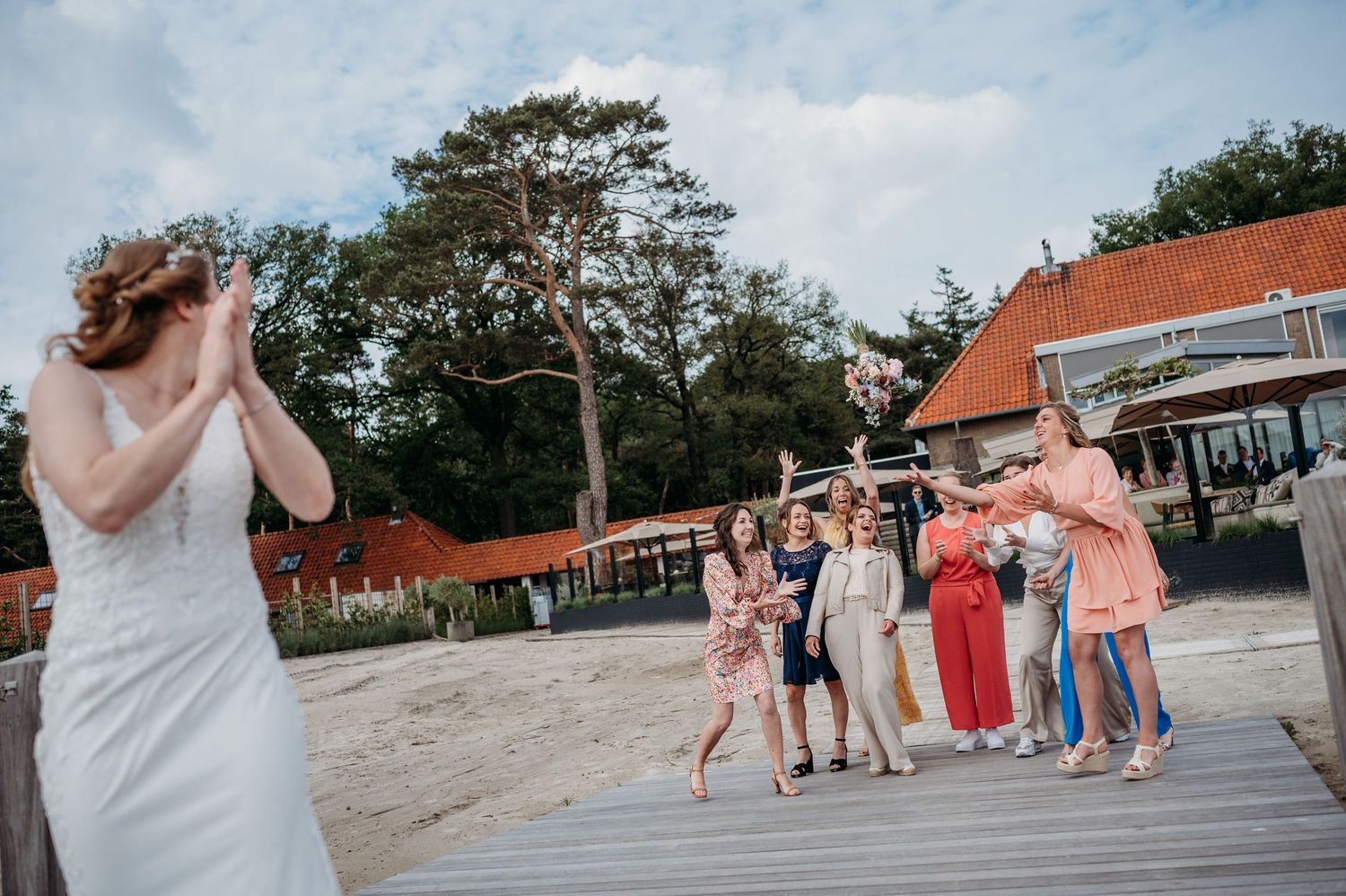 Gasten op houten dek terwijl bruid zich voorbereidt om boeket te gooien, bruidsfotografie IJM IJzereman Vught, Brabant.