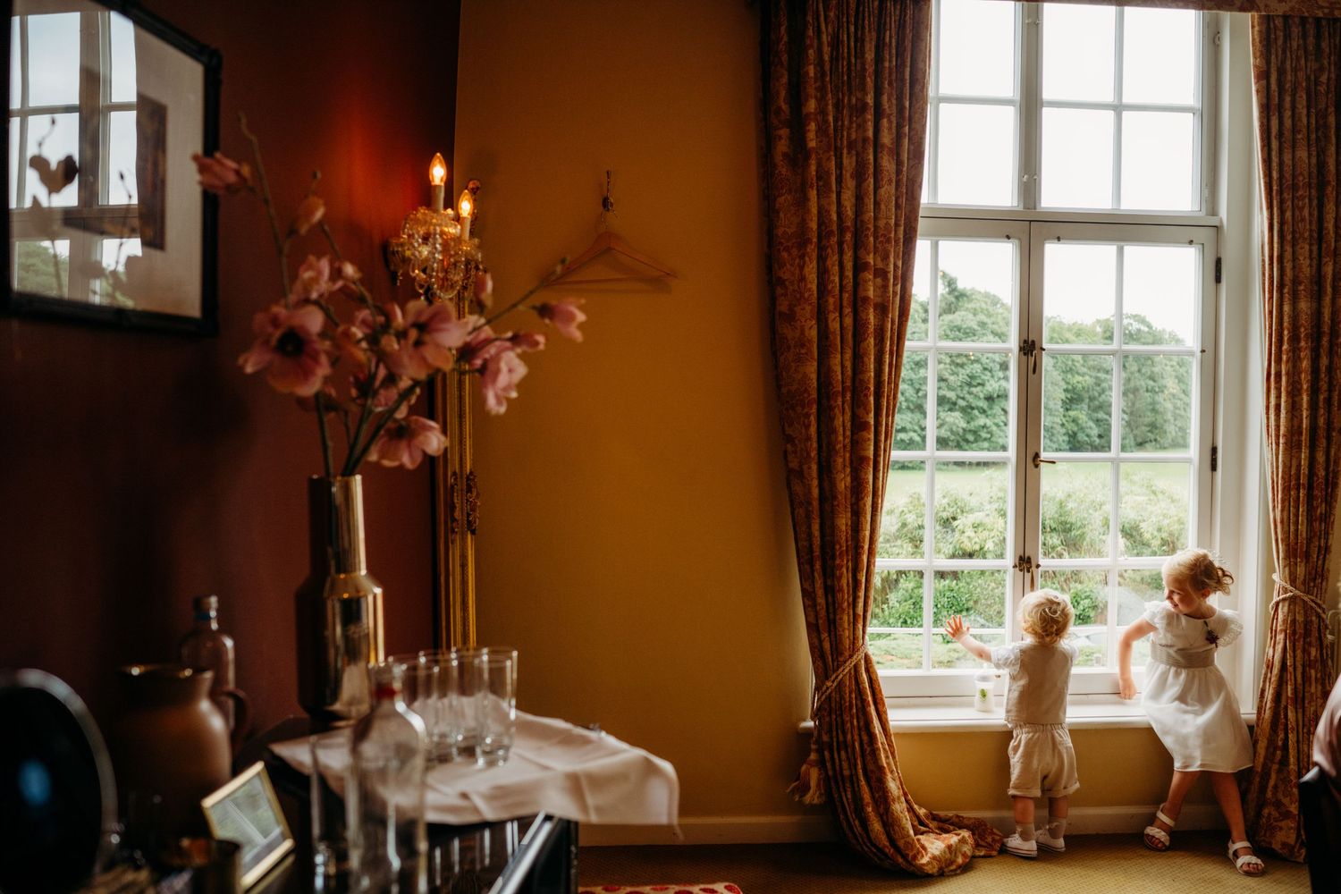 Elegante eetkamer met grote ramen en kinderen spelend in gouden middaglicht, bruidsfotografie Brabant