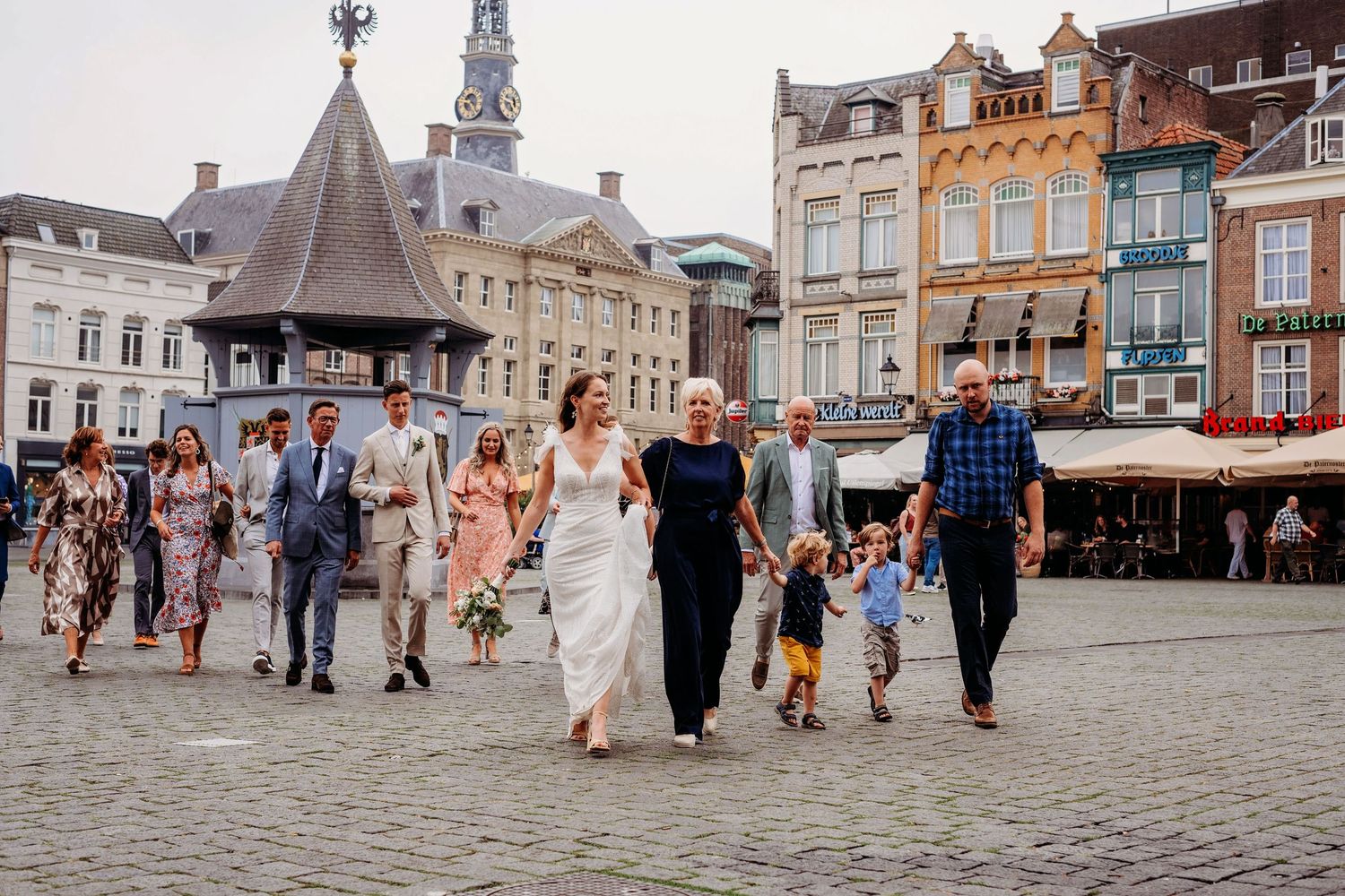 Bruidspaar en gasten lopen over de Markt in Den Bosch, spontane bruidsfotografie en trouwreportage in Brabant.
