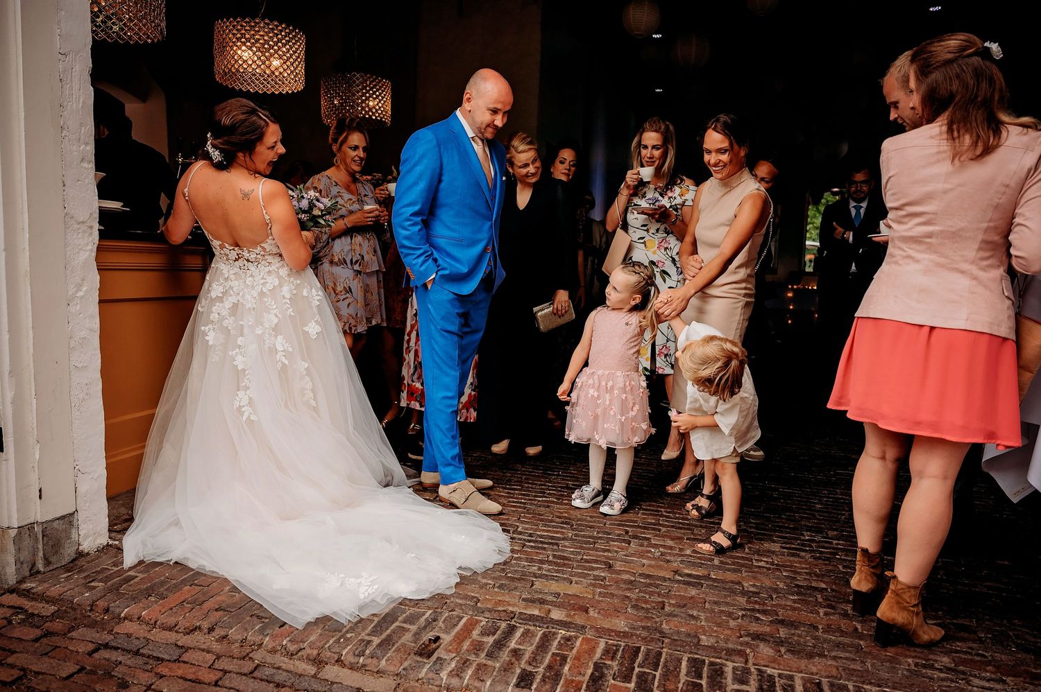 Bride and groom greet young flower girls and guests on a cobblestone path at their wedding.