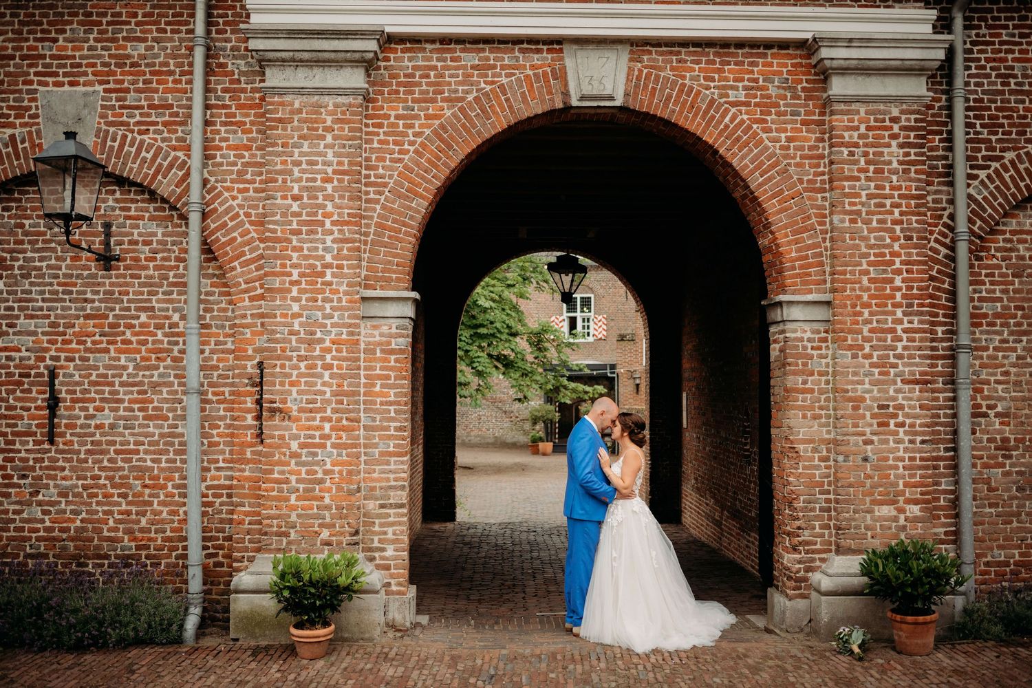 Bride and groom share romantic embrace under historic brick archway during wedding portrait session.
