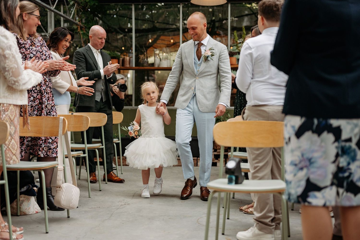 Groom walks down the aisle with a young flower girl in a white tutu dress.