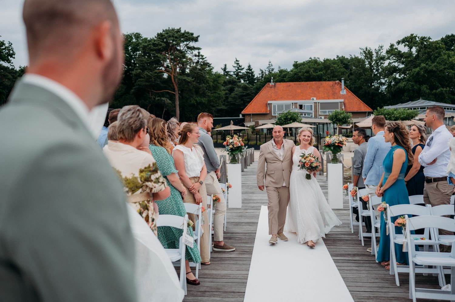 Buitenceremonie op houten steiger met witte stoelen en gasten, bruidsfotografie IJM IJzereman Vught, Brabant.