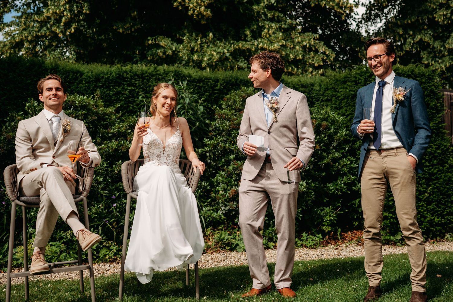 Bride and groom with groomsmen laughing outdoors at garden wedding ceremony in elegant attire.
