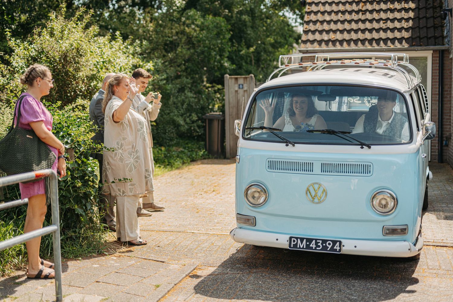 Vintage light blue VW camper van parked outside as wedding guests gather nearby.