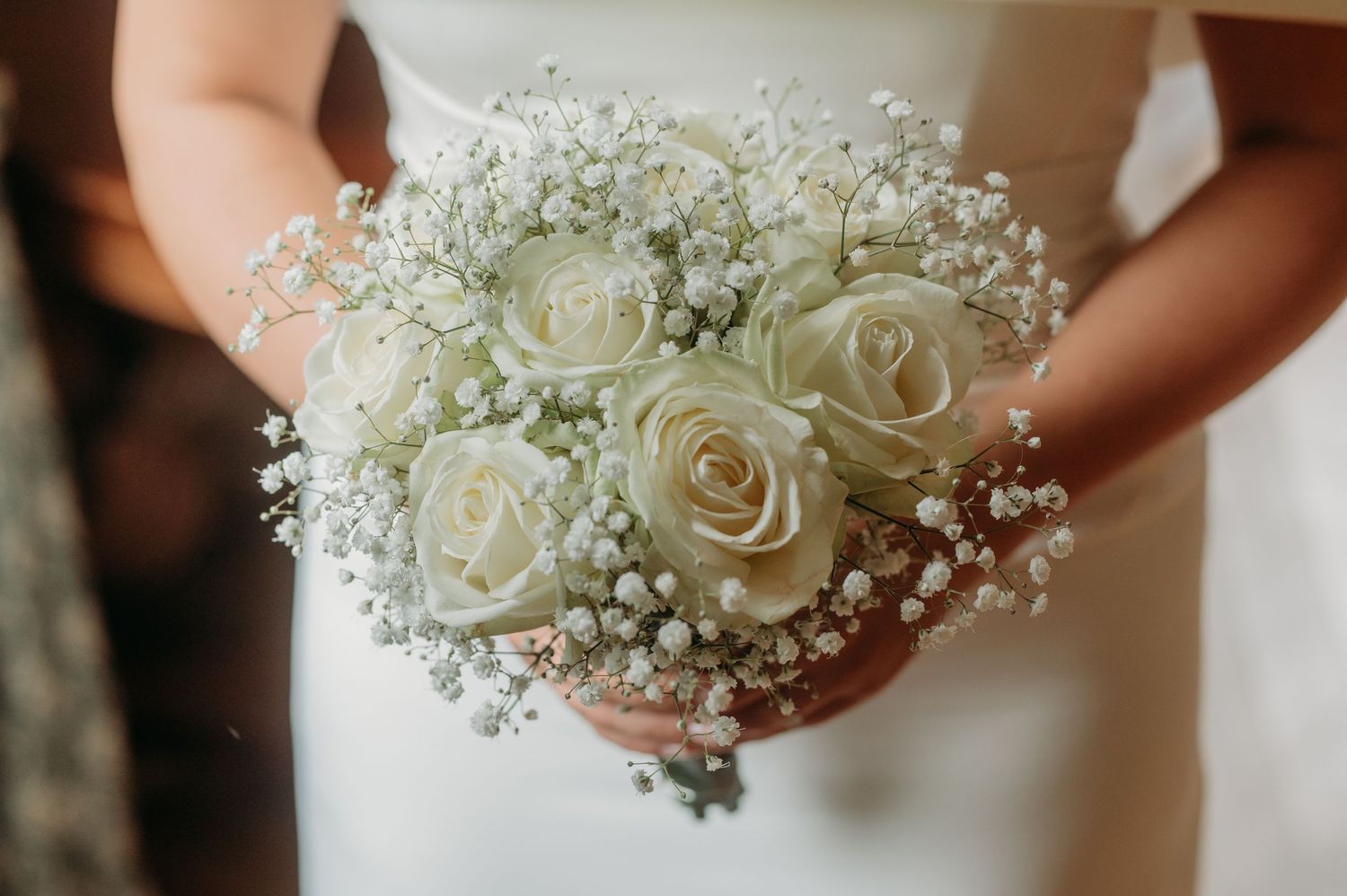 Bride holding a elegant wedding bouquet of white roses and baby's breath flowers in a classic bridal arrangement.