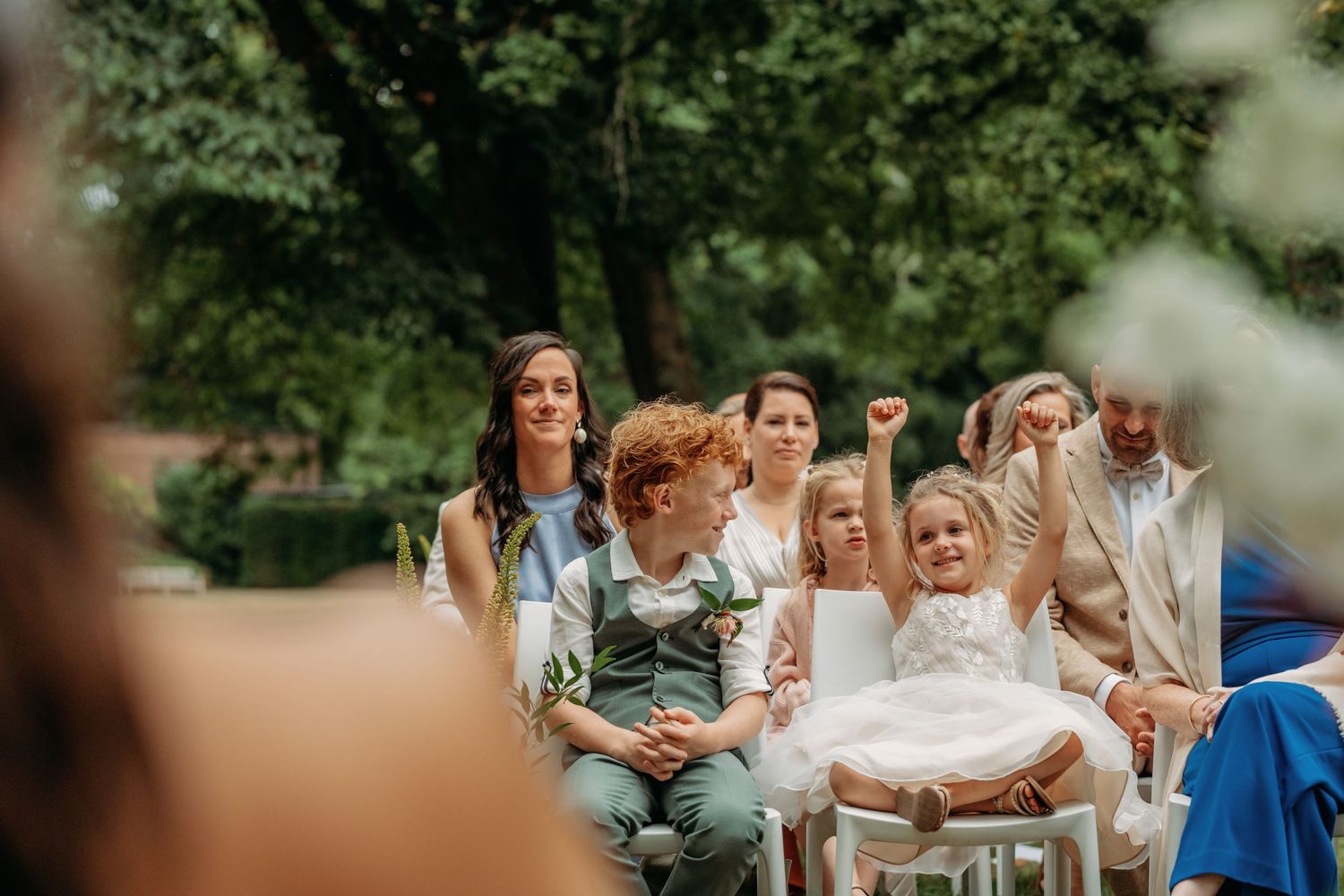 Bruiloftsgasten zittend op stoelen in een tuin tijdens een zomerse ceremonie, vastgelegd door bruidsfotograaf in Vught